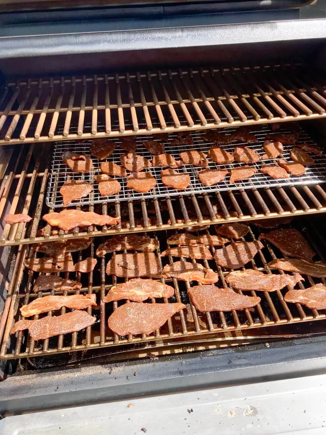 Slices of beef dehydrating on a smoker grill to make homemade beef jerky, a perfect high-protein snack for the carnivore diet.