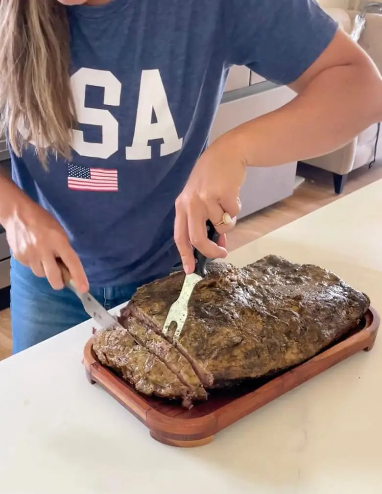 A woman slicing into a tender smoked brisket on a wooden cutting board, a delicious carnivore diet meal.