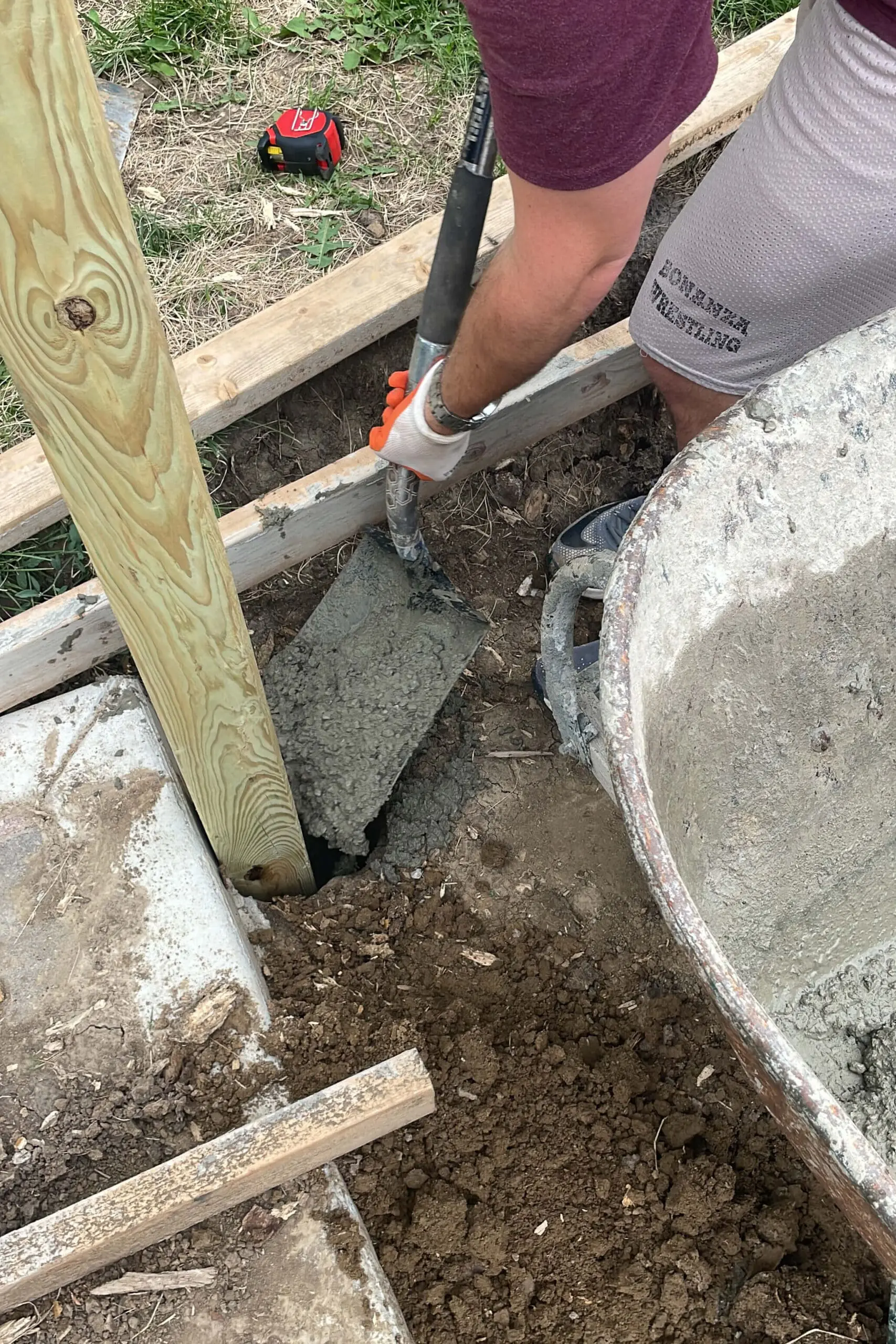 Concrete being poured around a 4x4 wood post to set it in place as part of a sturdy, freestanding privacy fence.
