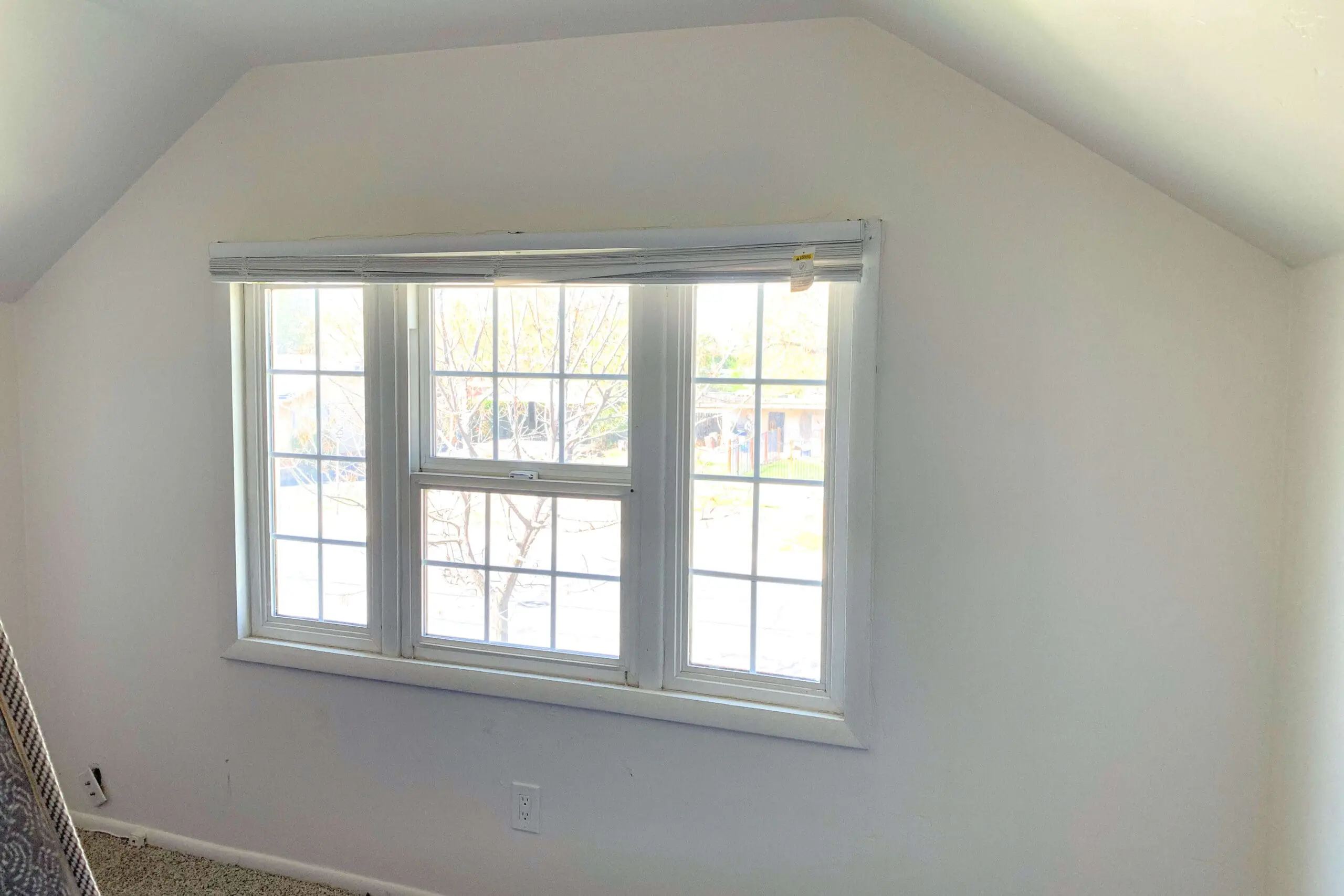 Plain white bedroom wall with windows before painting a DIY accent wall for a girl’s room makeover.