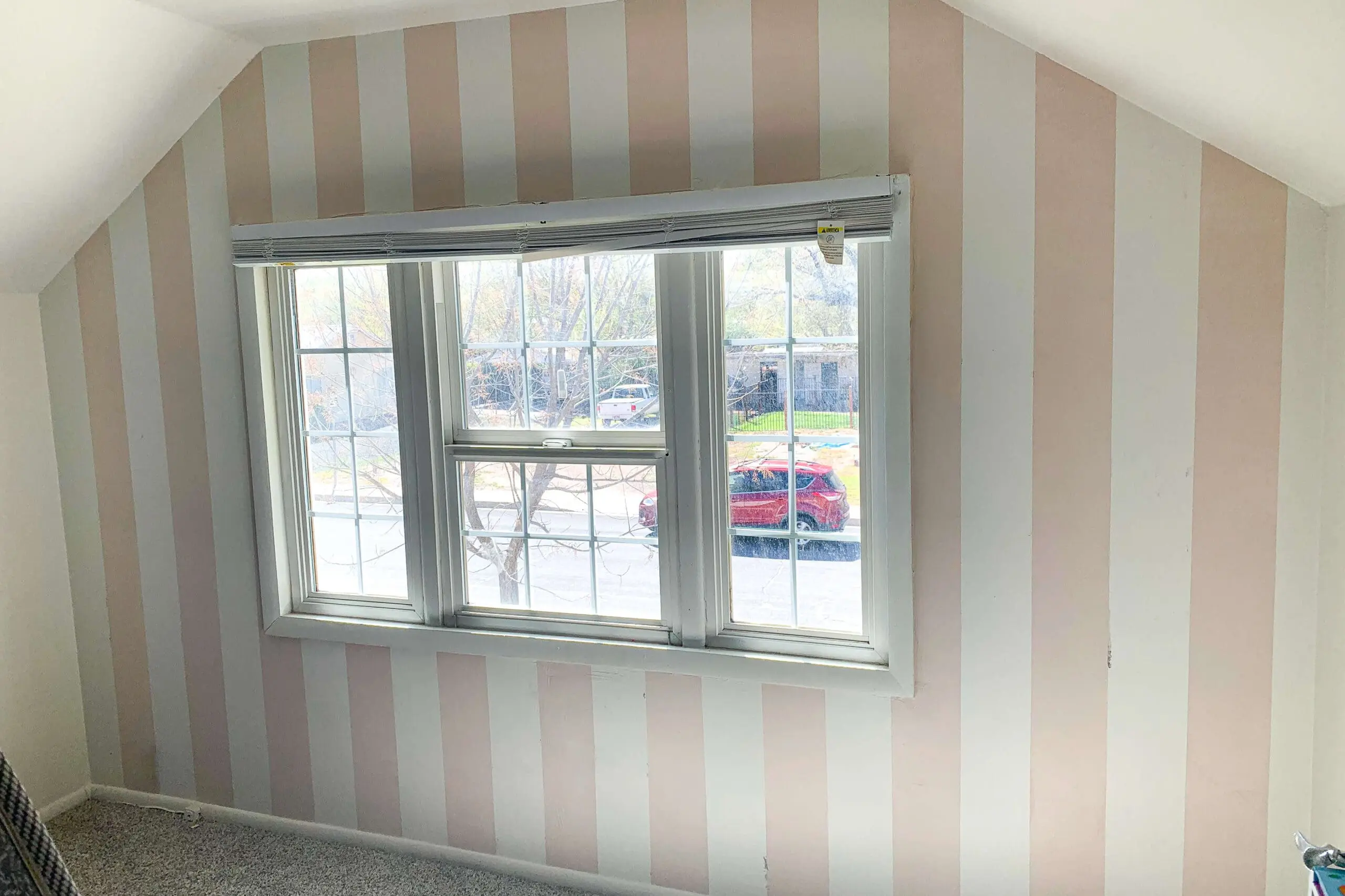 Completed vertical stripes in blush pink and white on a bedroom wall as the base layer for a DIY buffalo plaid pattern