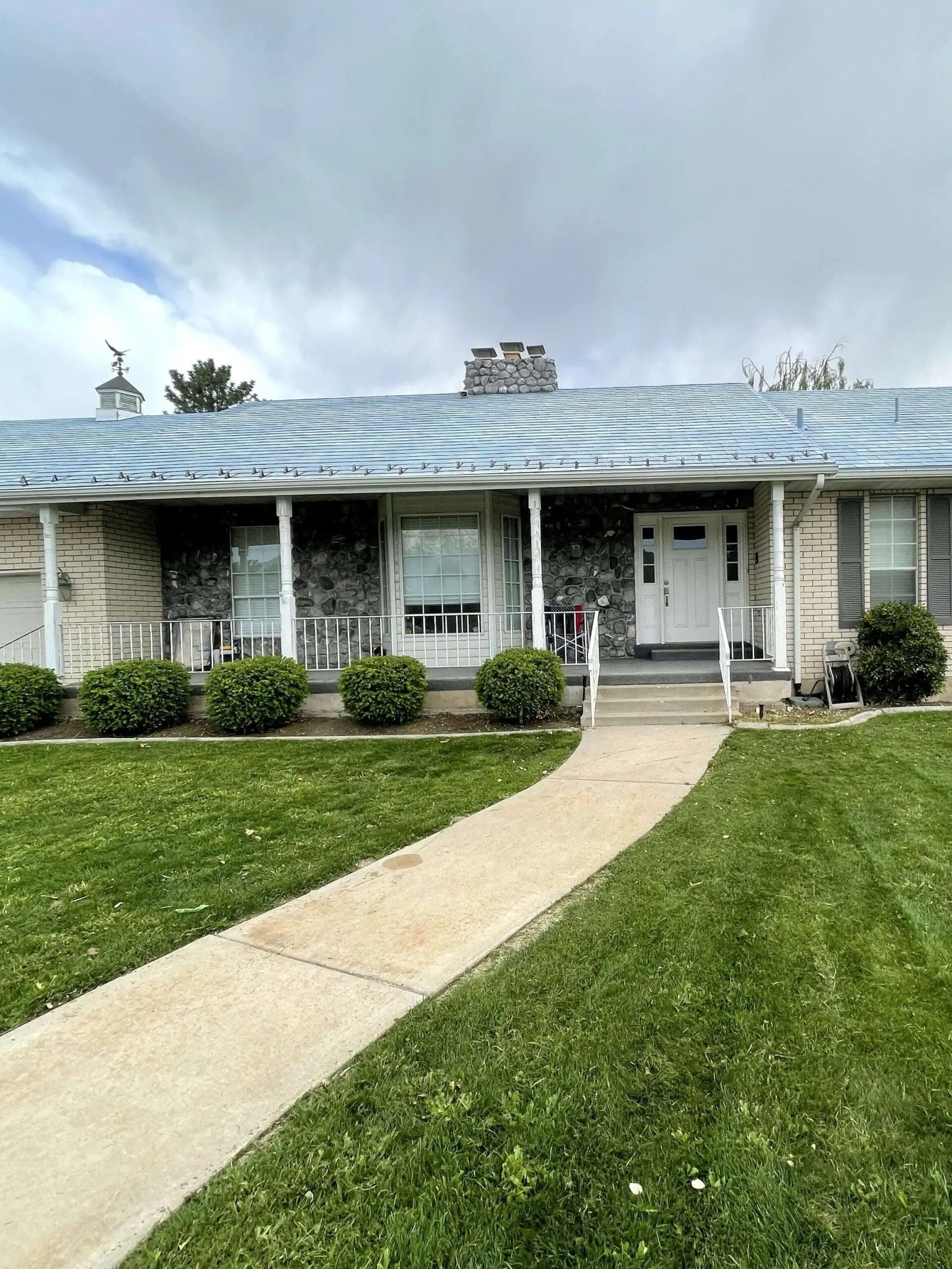 Full view of a ranch-style home with white brick, light blue roof, and white window grids before any updates.