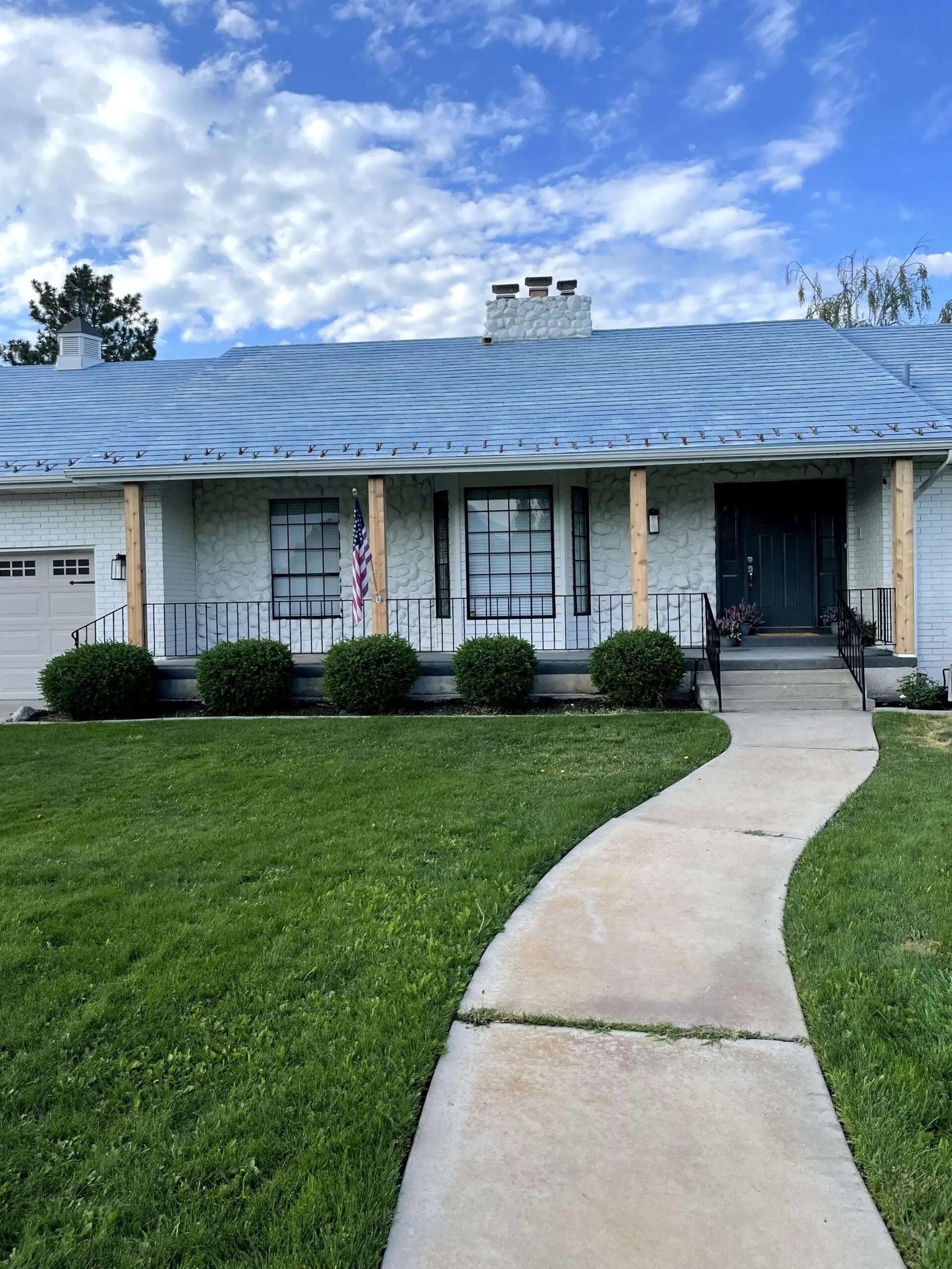 Updated exterior of a white brick home featuring black window grids, fresh wood porch posts, and a newly painted door.