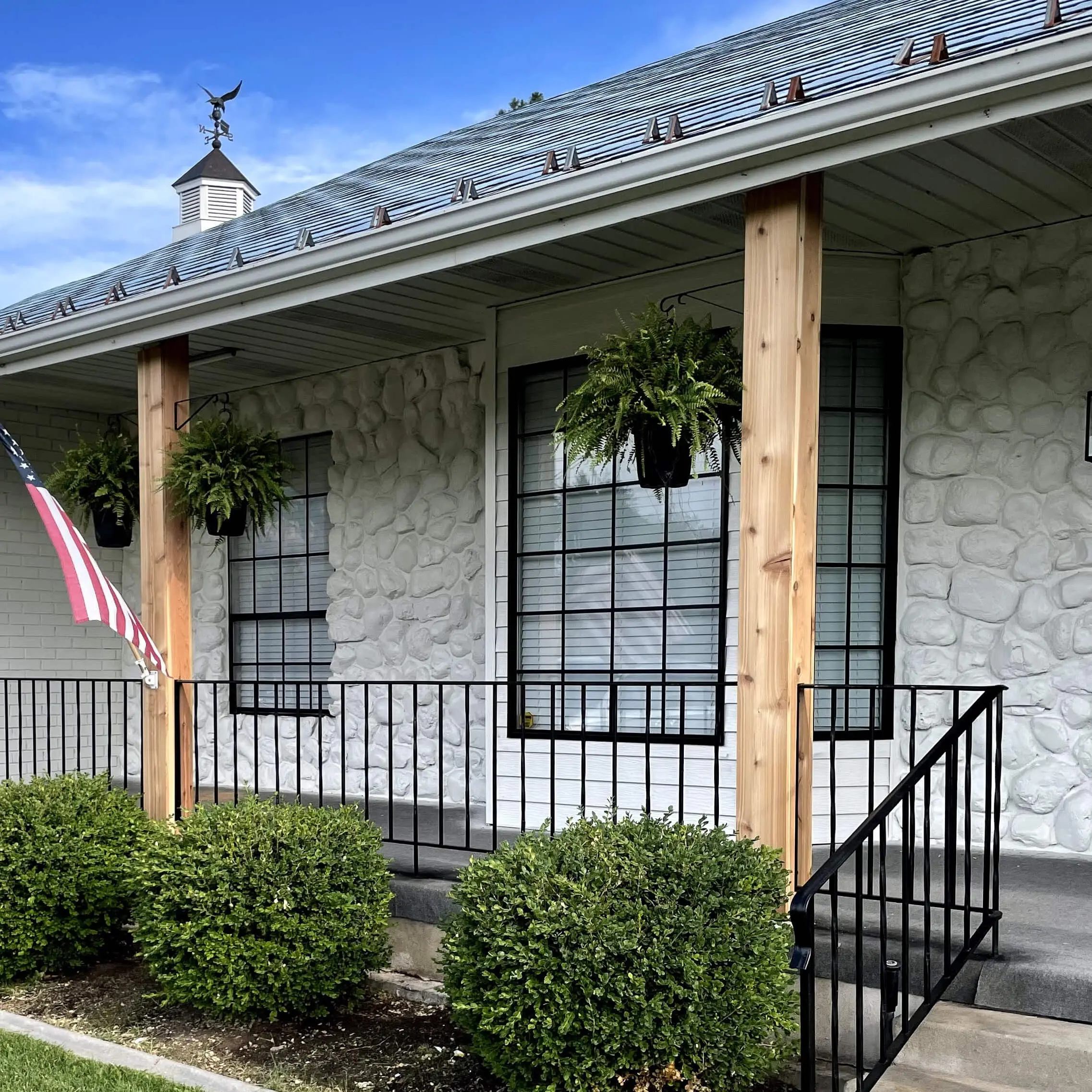Close-up of modern black window grids on a white painted stone exterior with fresh wood porch posts and black railing.