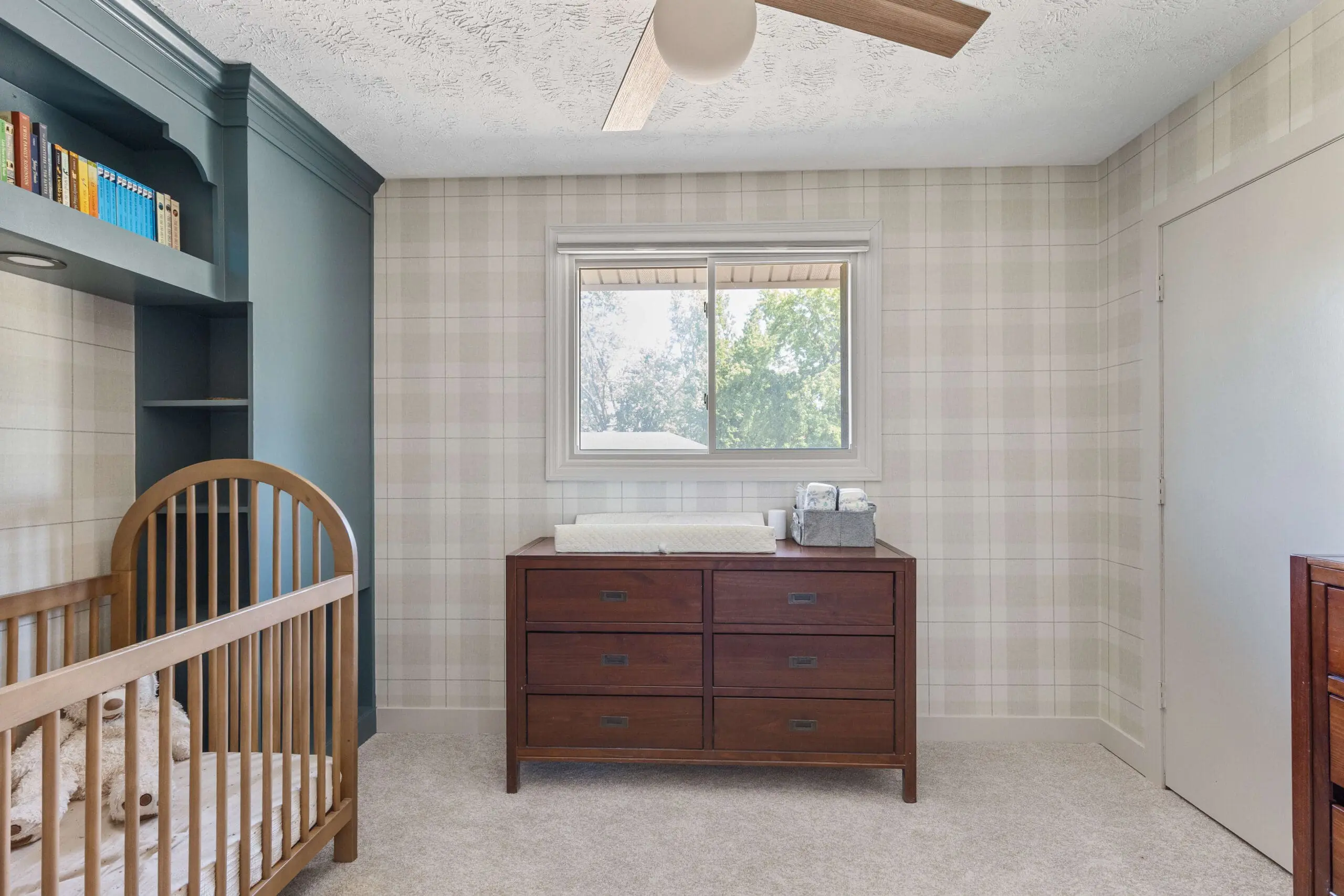 Changing table with storage drawers beneath a sunlit window in a plaid wallpaper nursery.