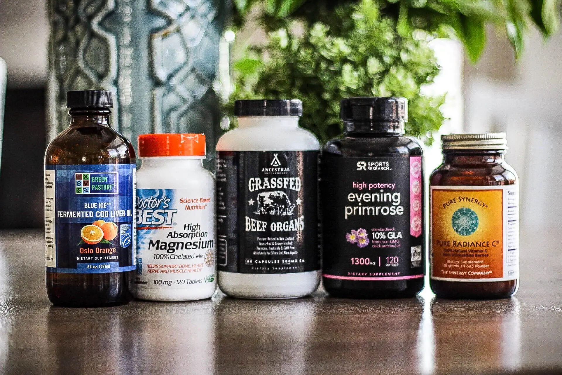Five bottles of whole-body wellness products on a table, featuring fermented cod liver oil, magnesium, beef organs, evening primrose, and a plant-based vitamin C blend.

