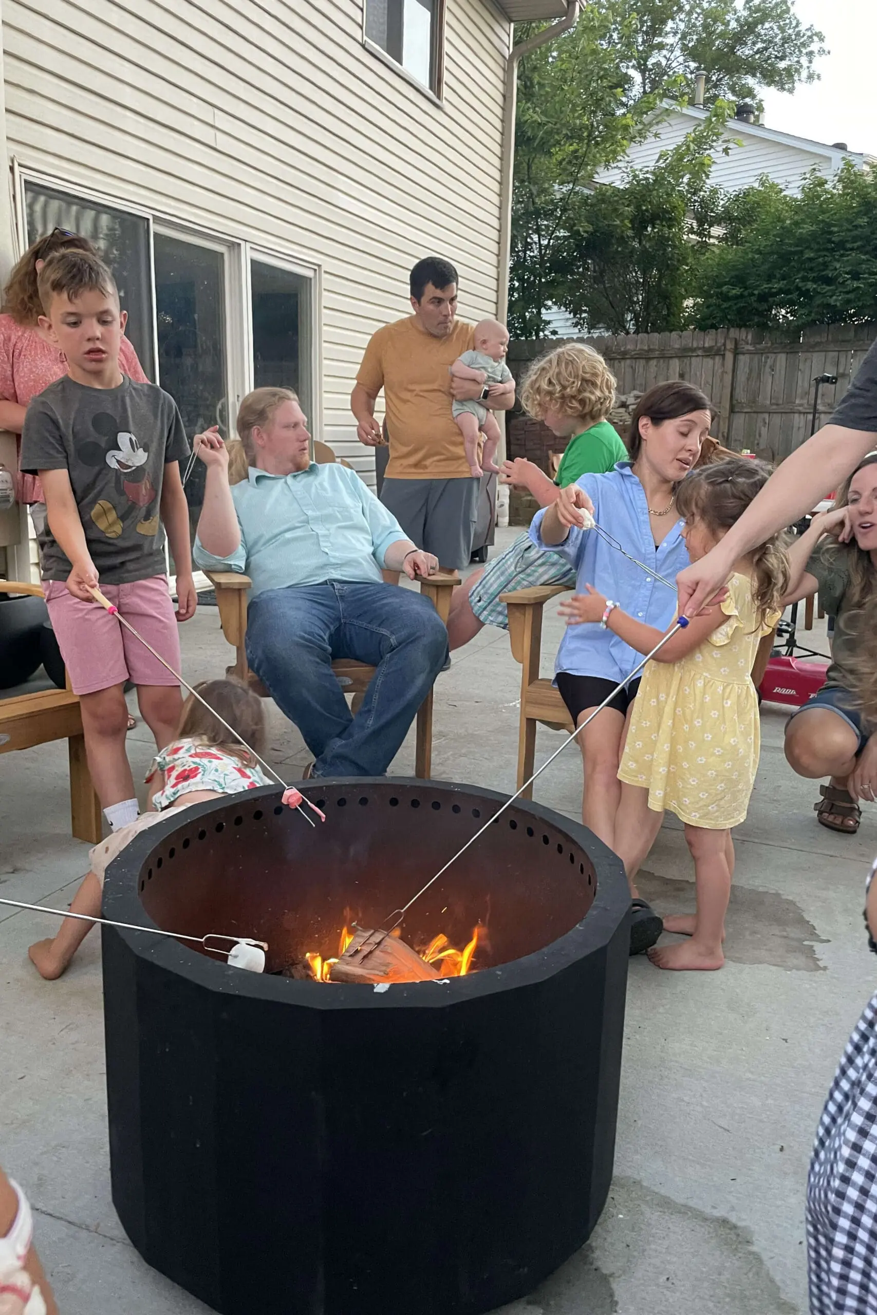Large family roasting marshmallows together around a backyard fire pit, perfect for relaxed summer nights and hosting loved ones.