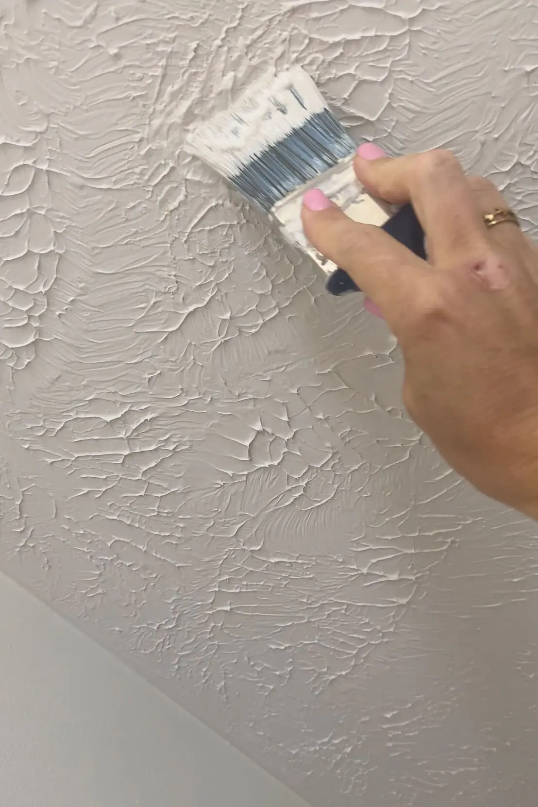 Hand using a brush to paint over patched texture on a white ceiling