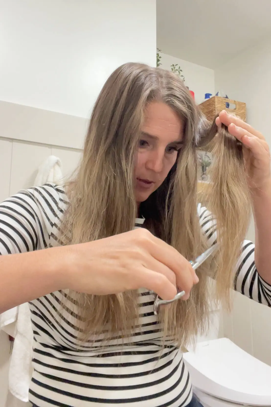 Focused DIY haircut in progress, trimming a mid-length section for blended layers.