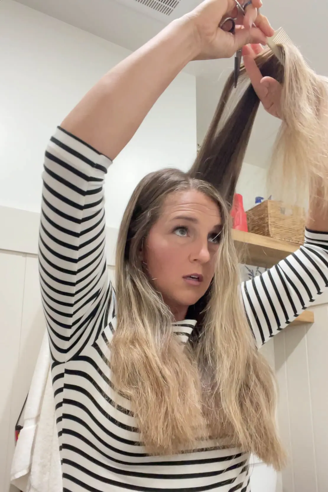 Woman holding a section of hair straight up while trimming top layers during a DIY haircut at home.