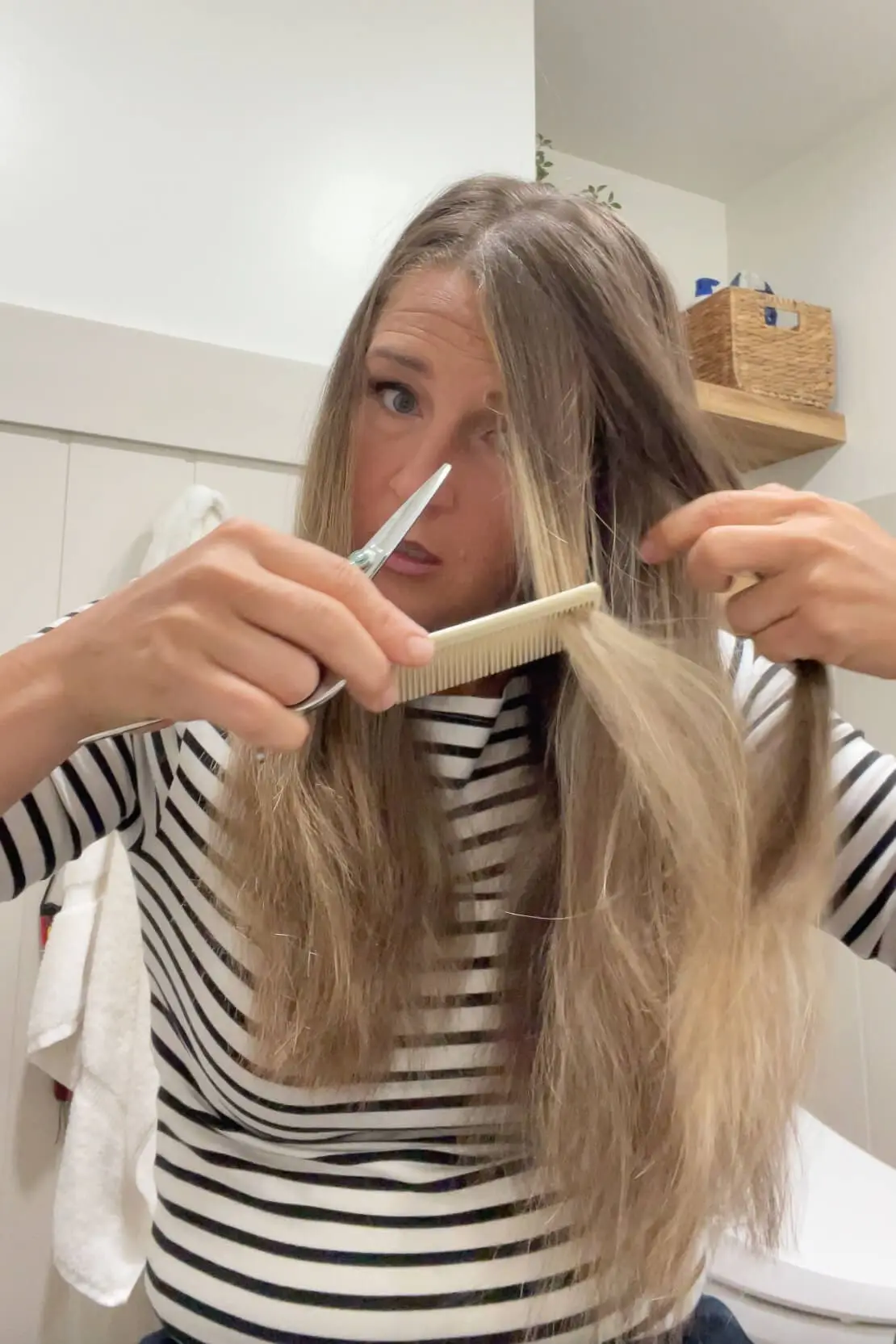 Using a comb and scissors to trim face-framing layers in long straight hair at home.