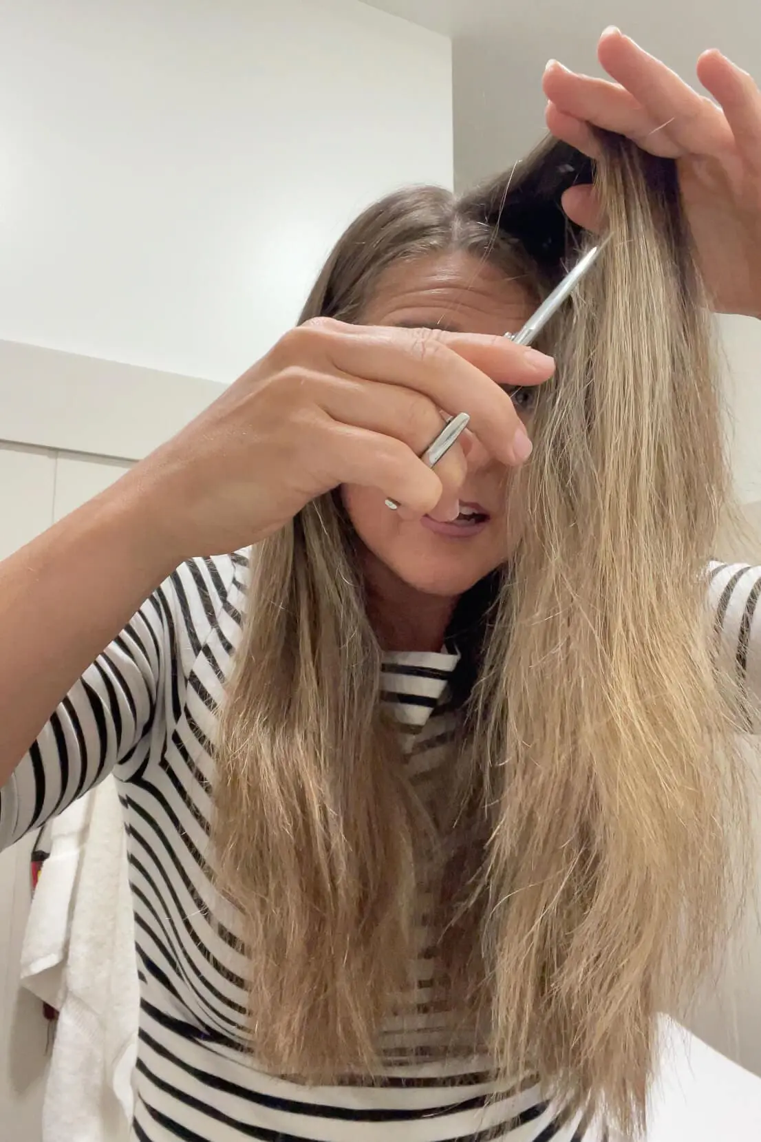 Trimming a section of hair using point-cutting technique to soften layers during a DIY haircut.