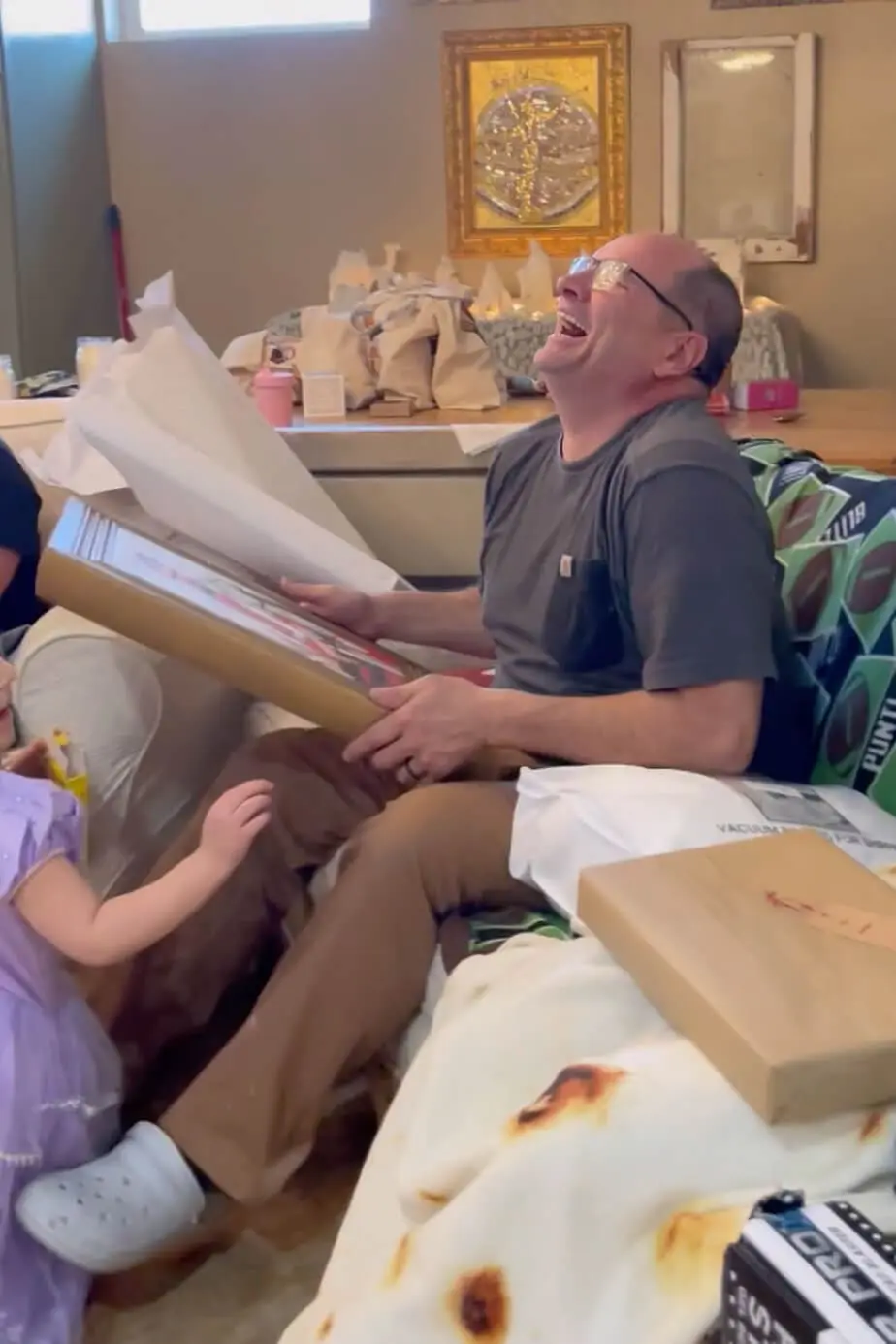 Father laughing while unwrapping a homemade canvas portrait gifted for Father's Day.