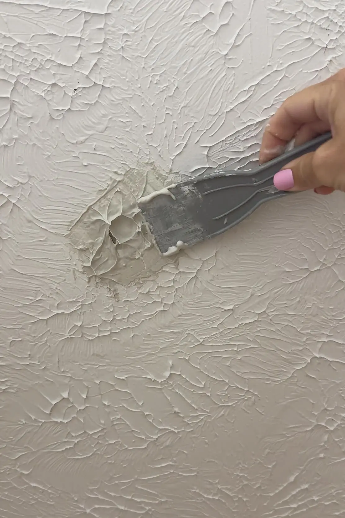 Applying joint compound over a ceiling hole using a putty knife to blend with textured surface