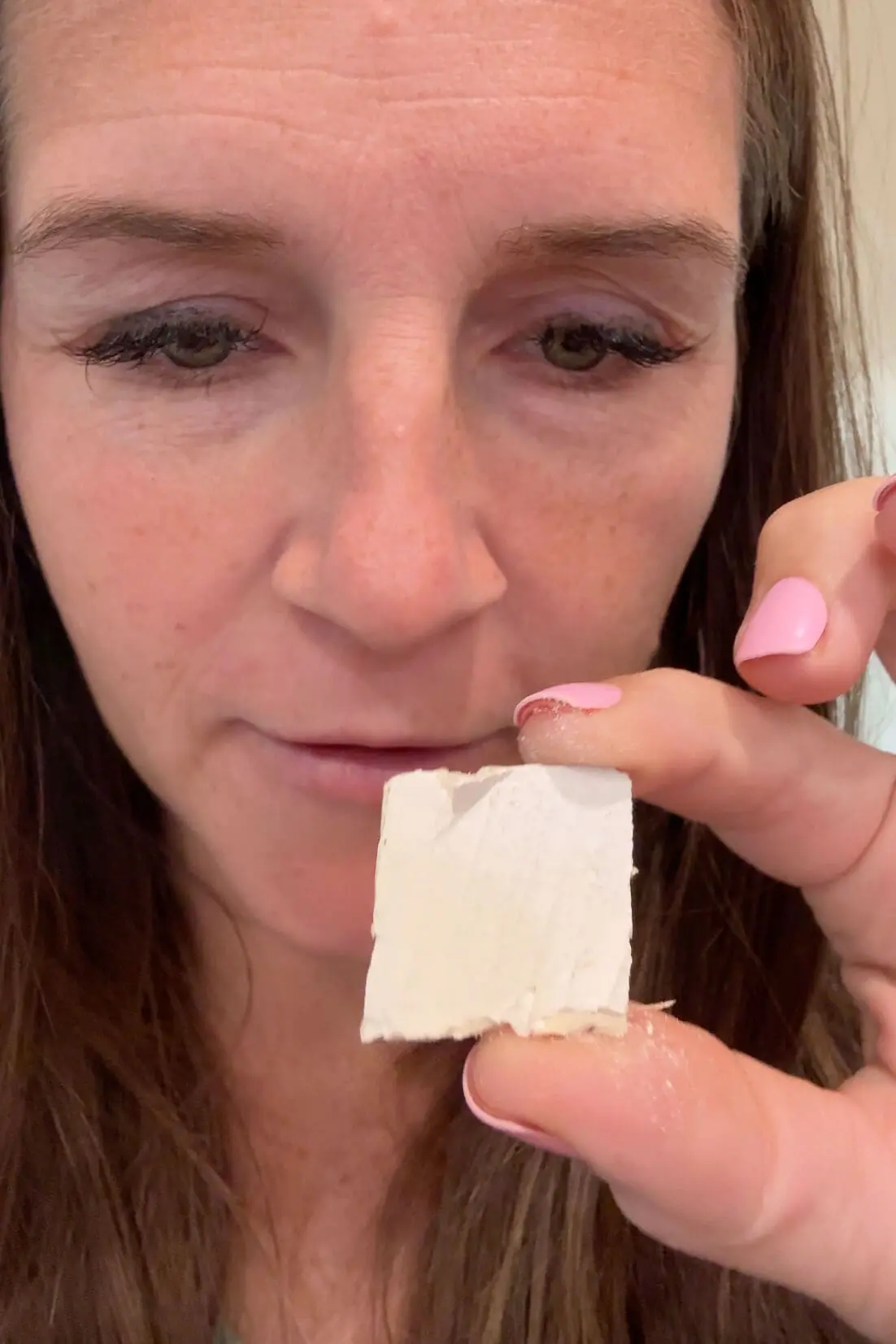 Close-up of a woman holding a small piece of painted drywall to match ceiling paint color