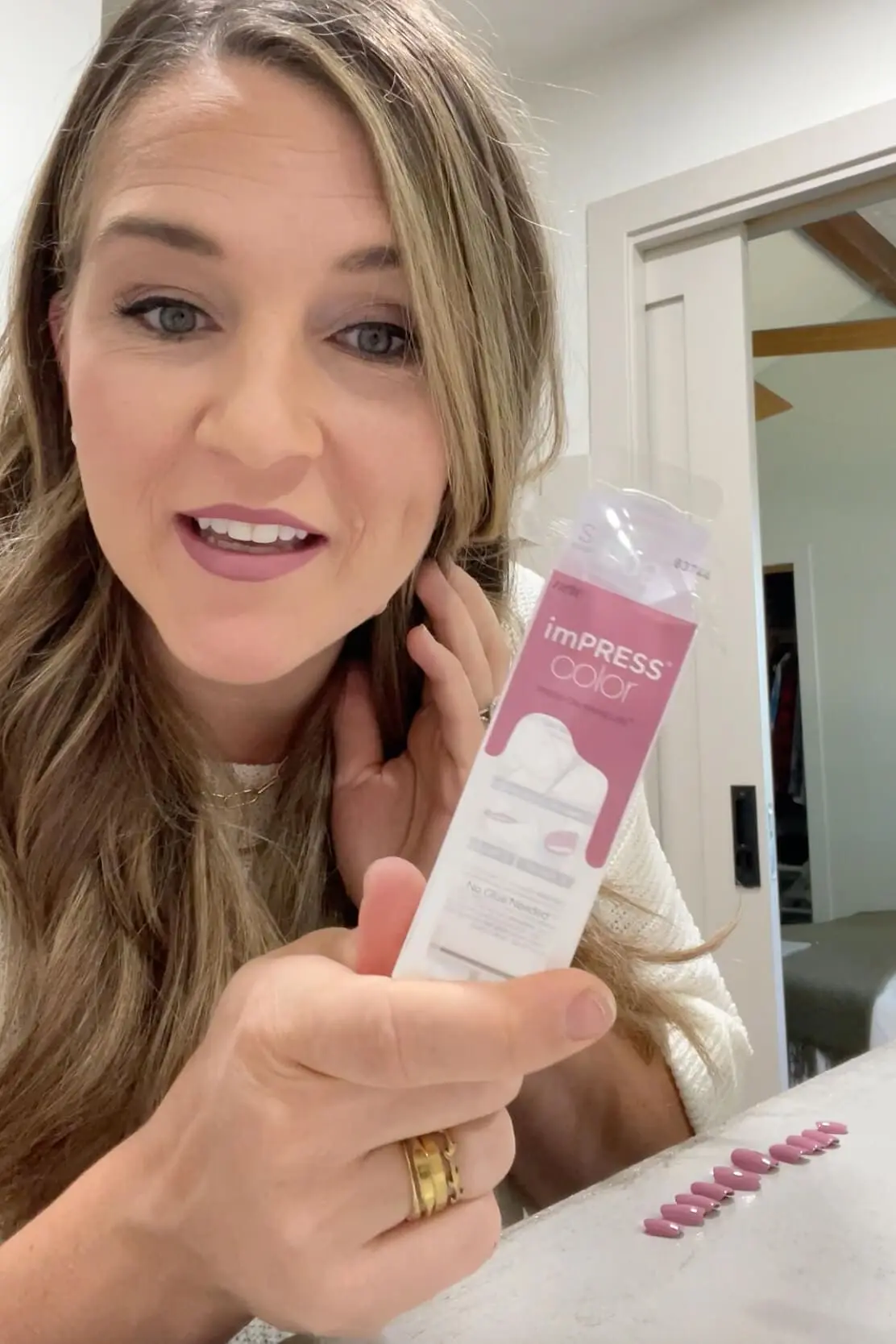 Holding a package of Kiss Impress Nails with a full set laid out on the counter, ready for a step-by-step press-on manicure tutorial.