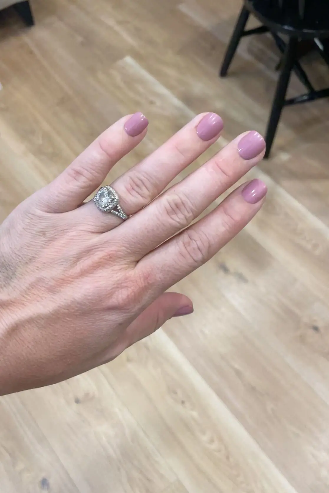 Hand wearing Kiss Impress nails in a soft mauve shade called petal pink, photographed against light wood flooring for a natural at-home manicure look.