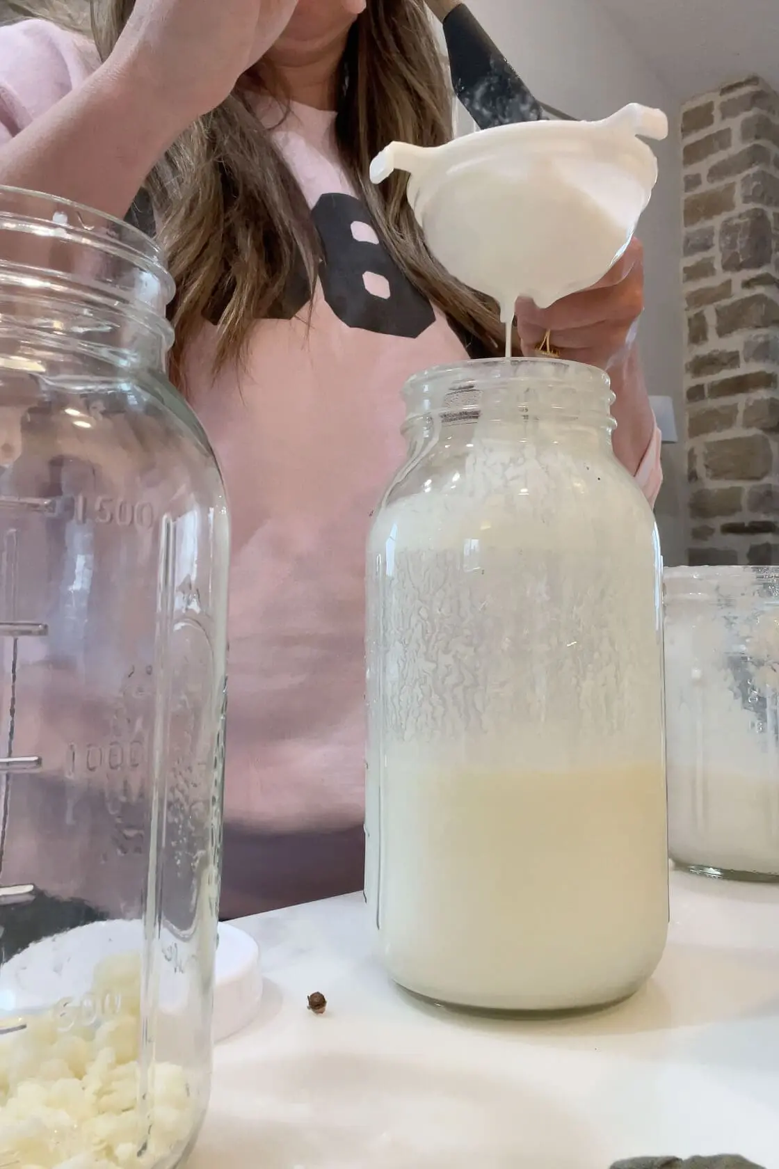 Straining thick homemade kefir into a mason jar to separate the grains—an important step in how to make milk kefir at home.