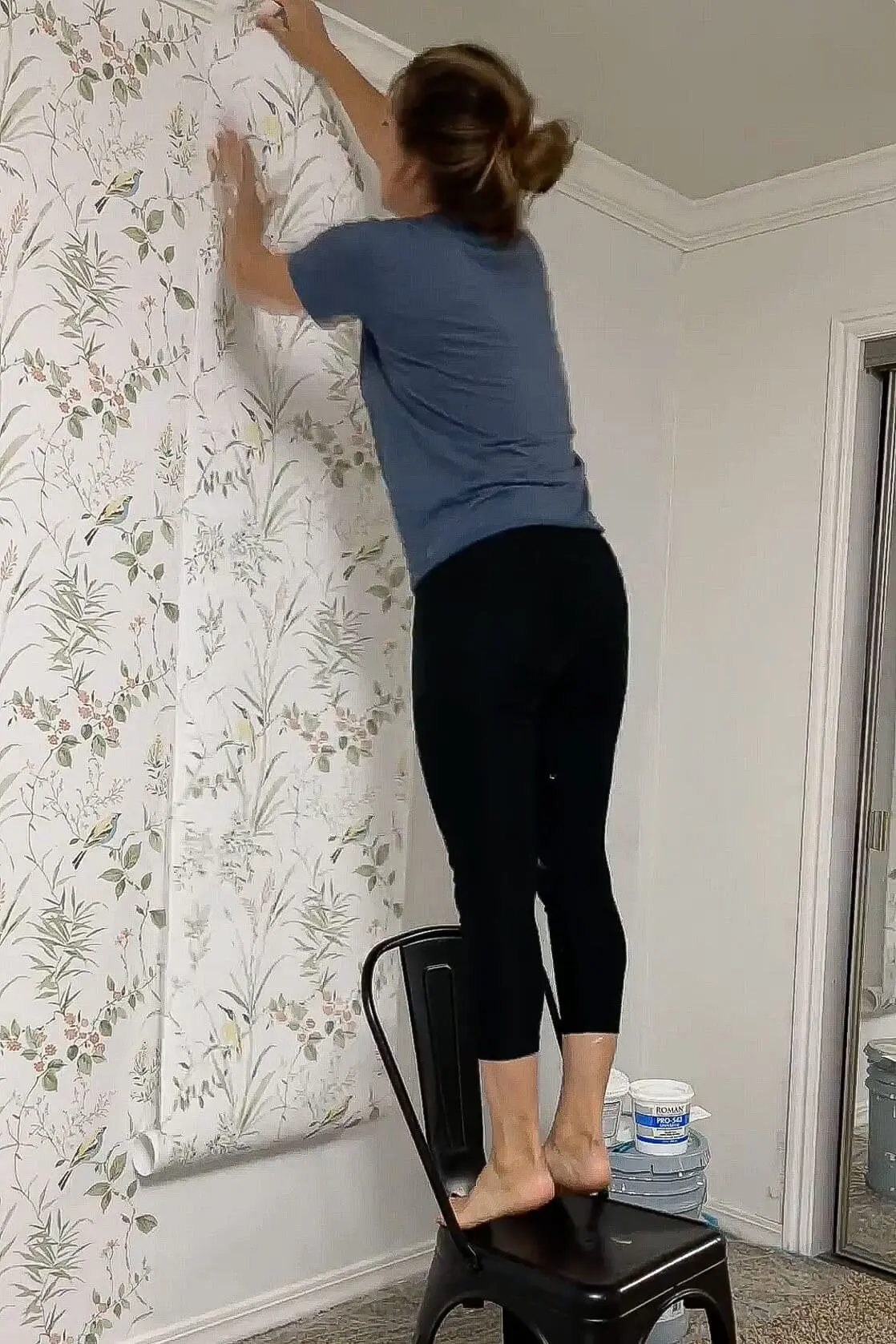 Pressing a new panel of traditional wallpaper into place while standing on a chair