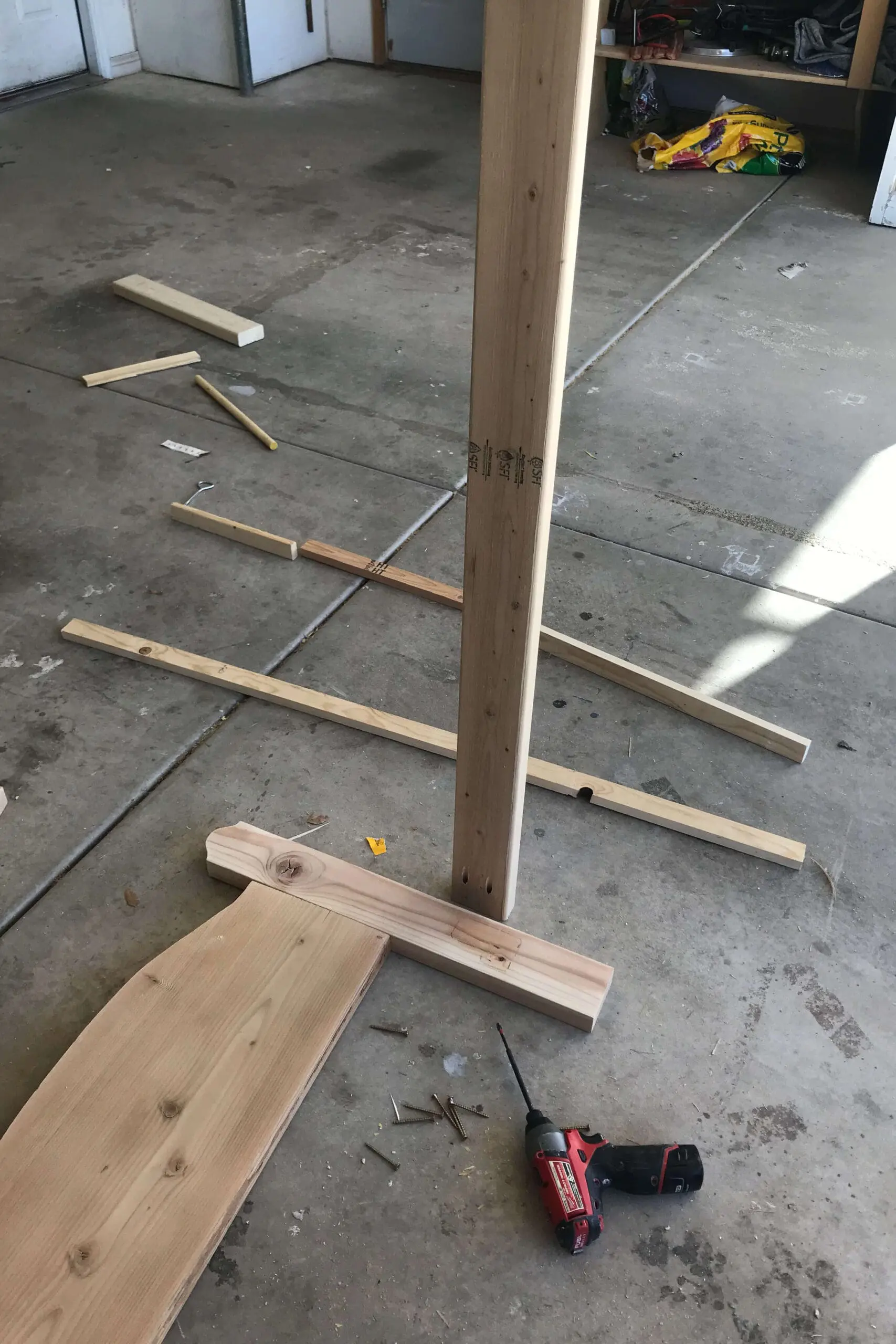 Close-up of pocket hole screws securing the leg posts to the curved headboard during DIY bed assembly, with drill and hardware nearby.