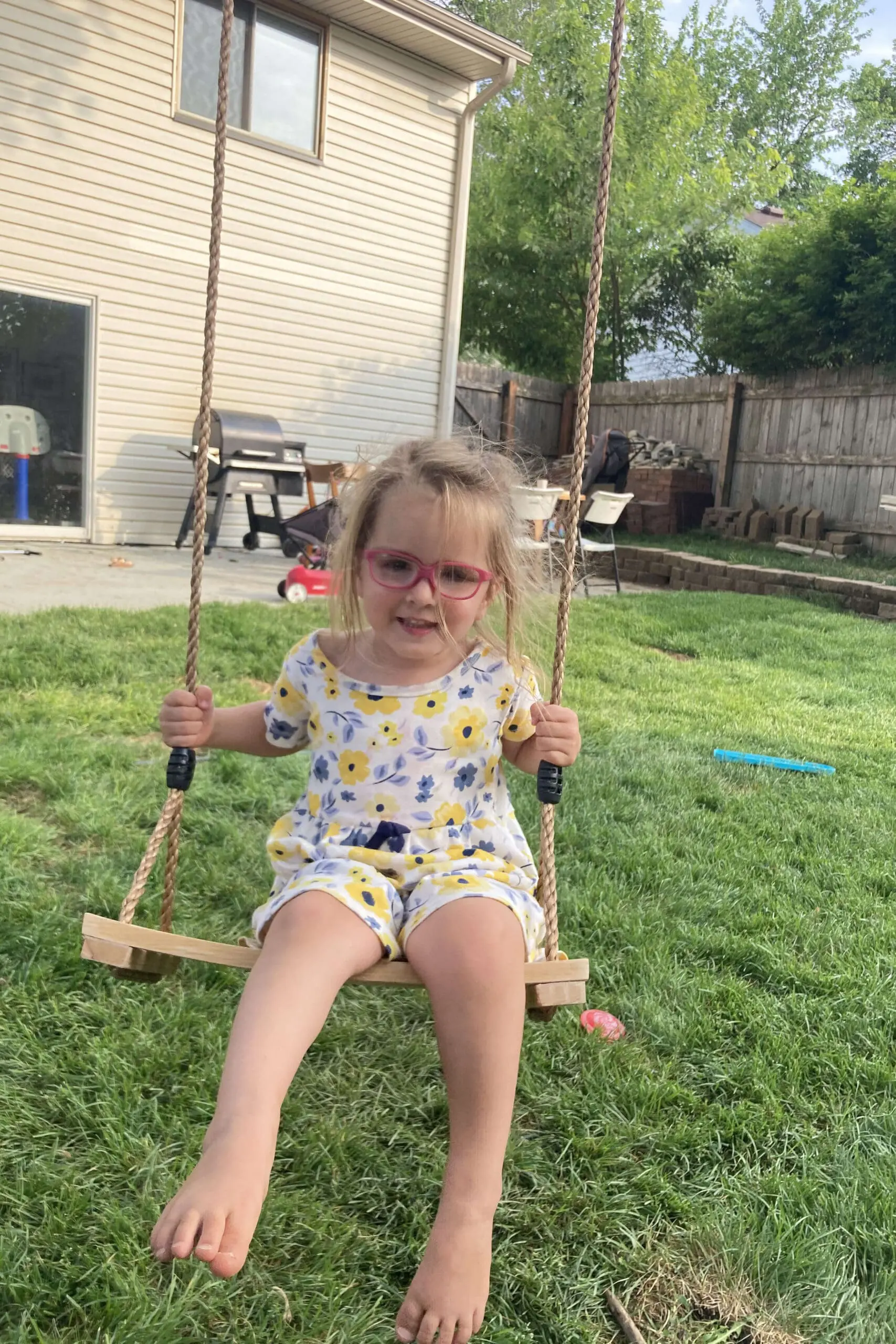 Child swinging barefoot in the yard on a DIY wooden tree swing, enjoying a summer afternoon.