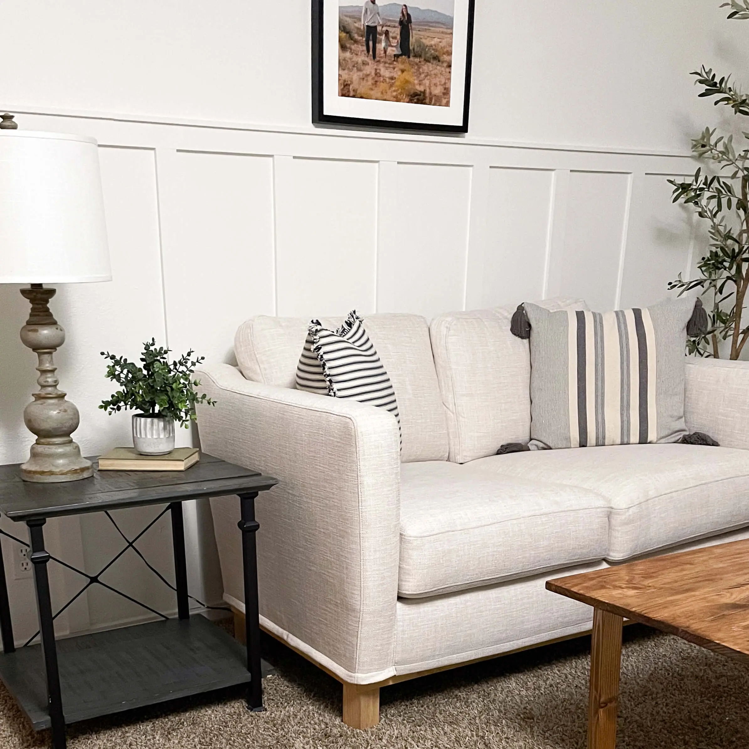 Neutral living room with a white batten feature wall behind a cream-colored sofa, accented with striped throw pillows and a cozy side table vignette.