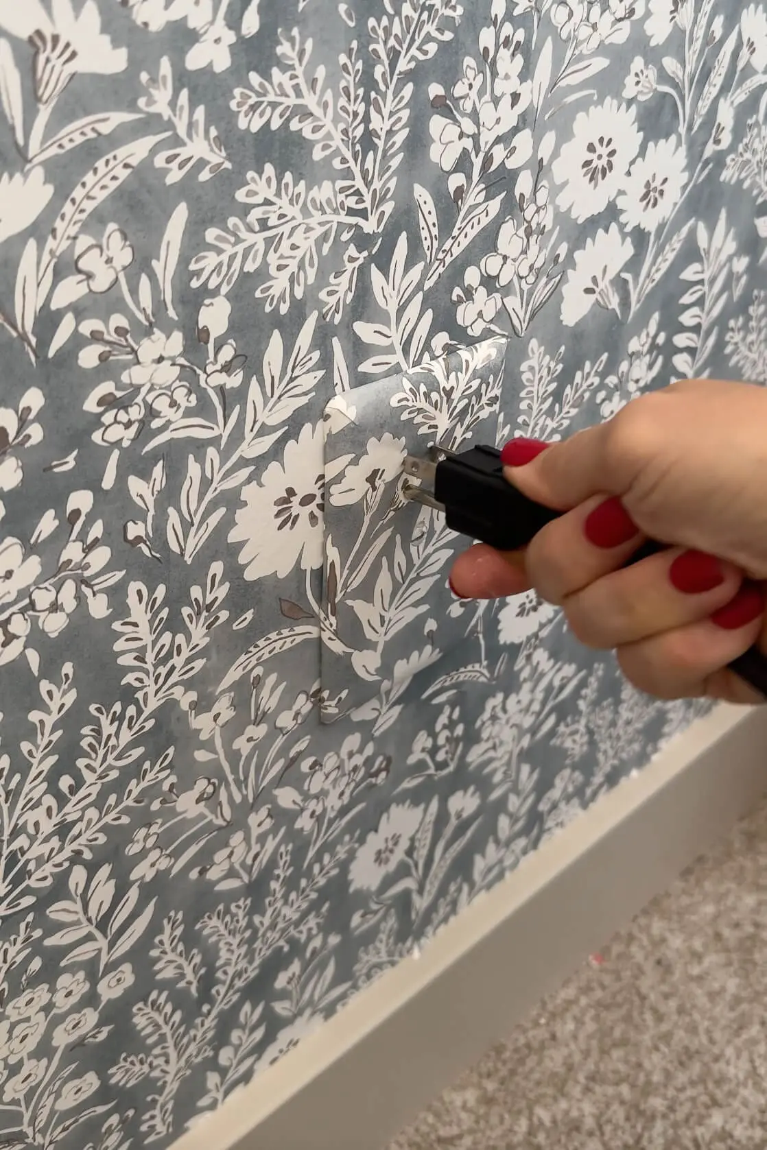 An electrical cord being plugged into a camouflaged outlet cover that blends perfectly into the wallpaper, creating a hidden outlet effect.