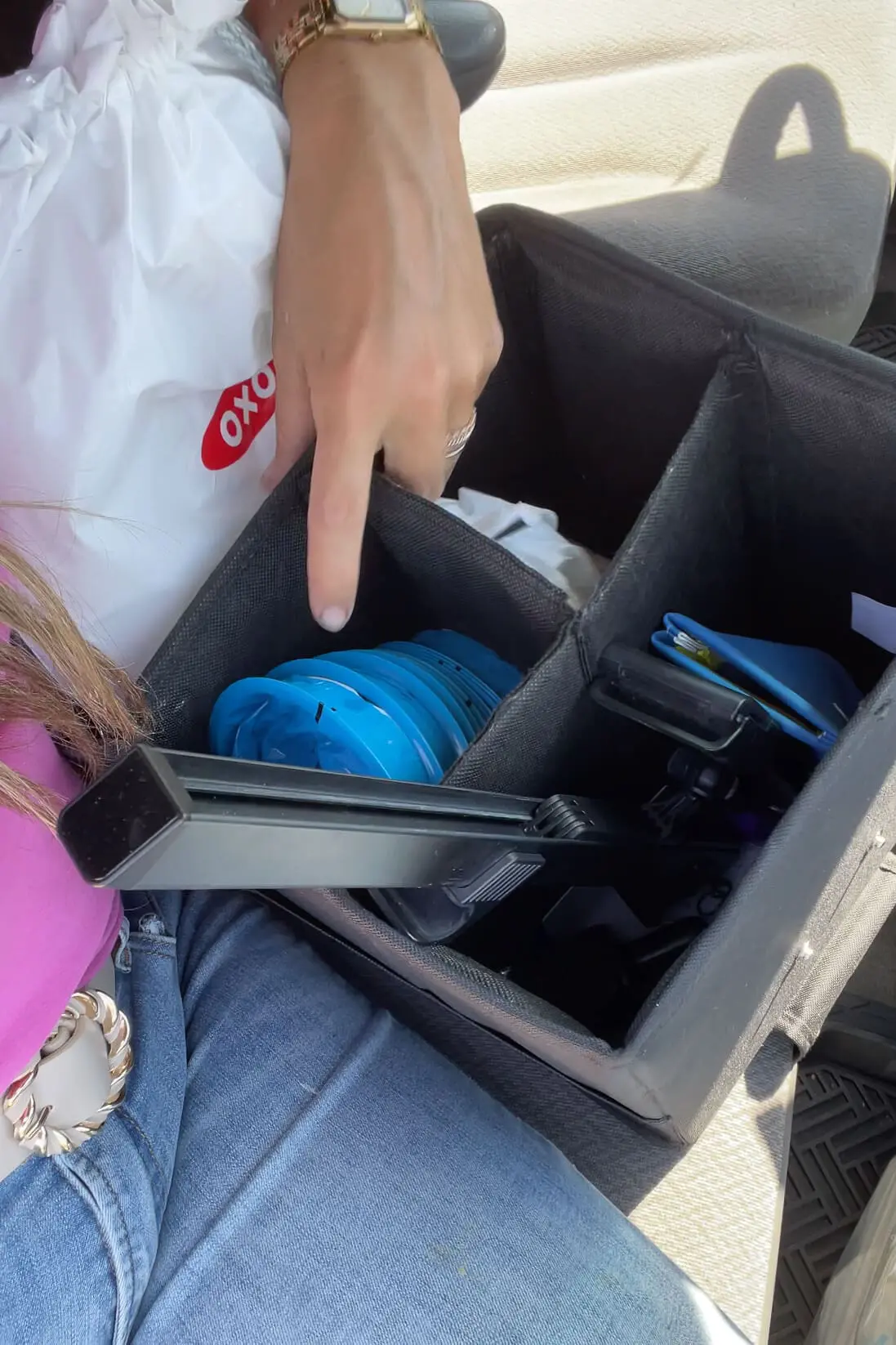 Close-up of a hand pointing to a stack of blue barf bags neatly packed in a car seat organizer alongside other road trip items.