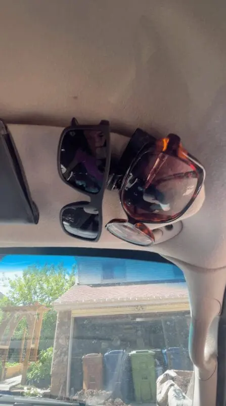Close-up of a sunglasses clip mounted to the car’s visor, holding multiple pairs of sunglasses securely for easy access while driving.