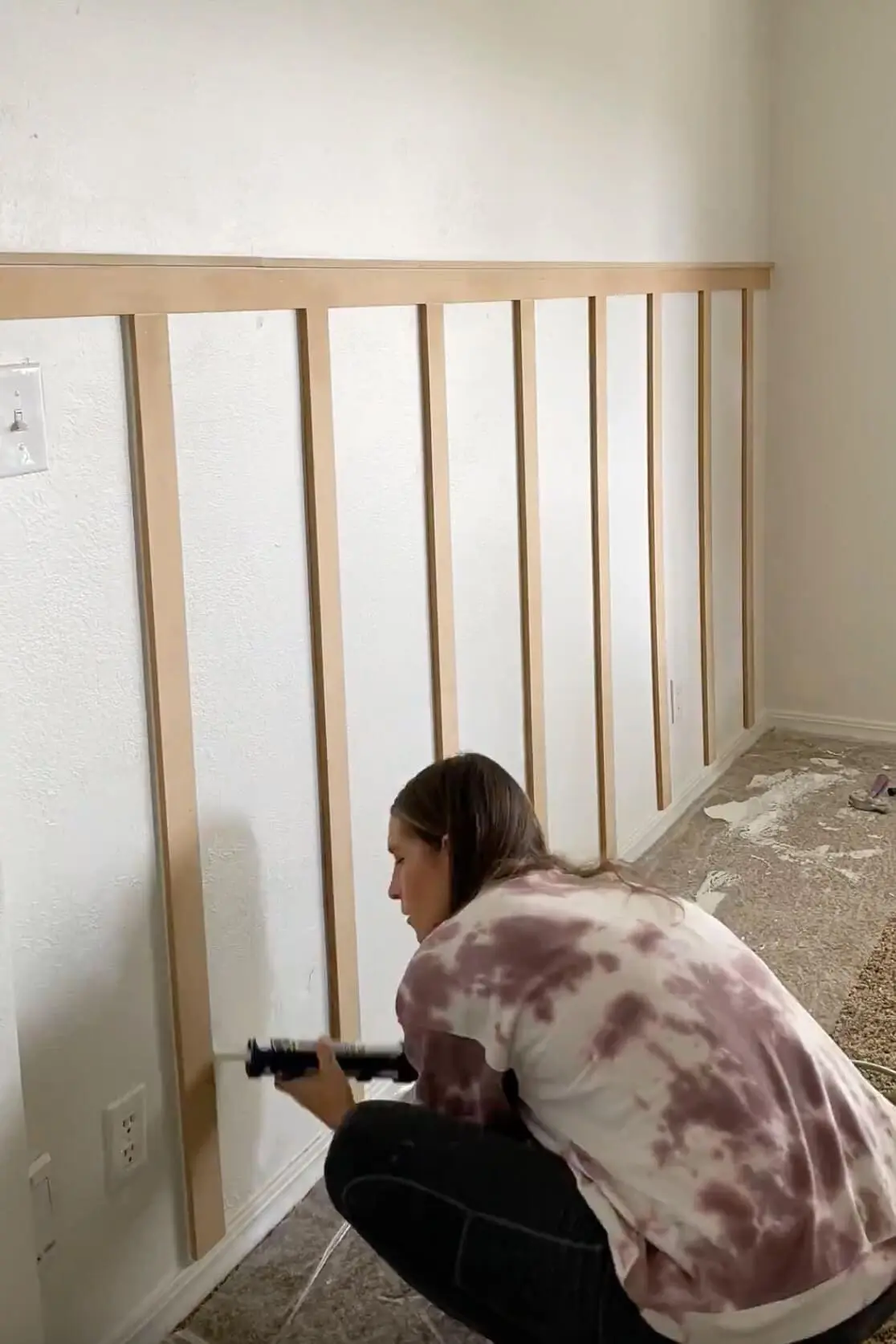 Applying caulk along the seams of vertical battens to prep for painting a clean and polished accent wall.