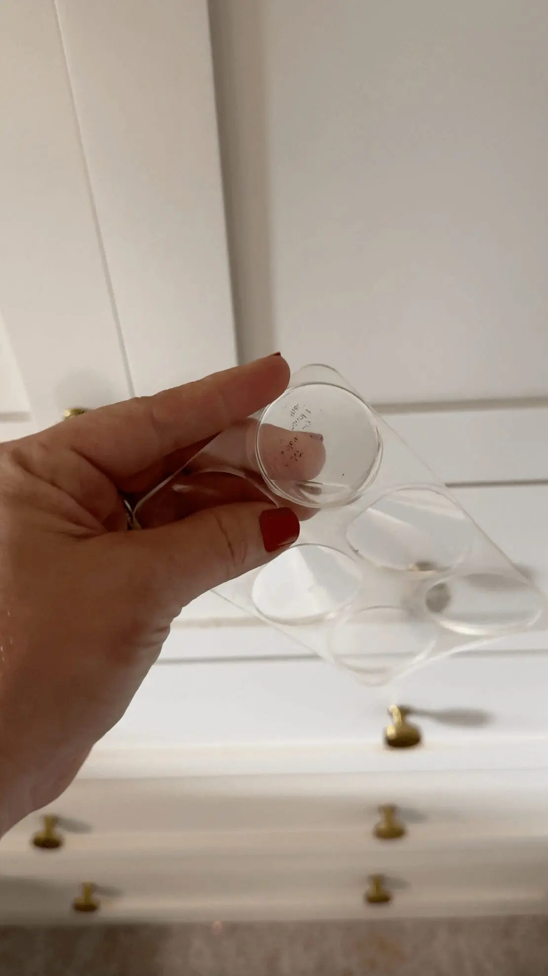 Hand holding a clear adhesive bumper designed to protect wallpaper from cabinet knobs or door handles.