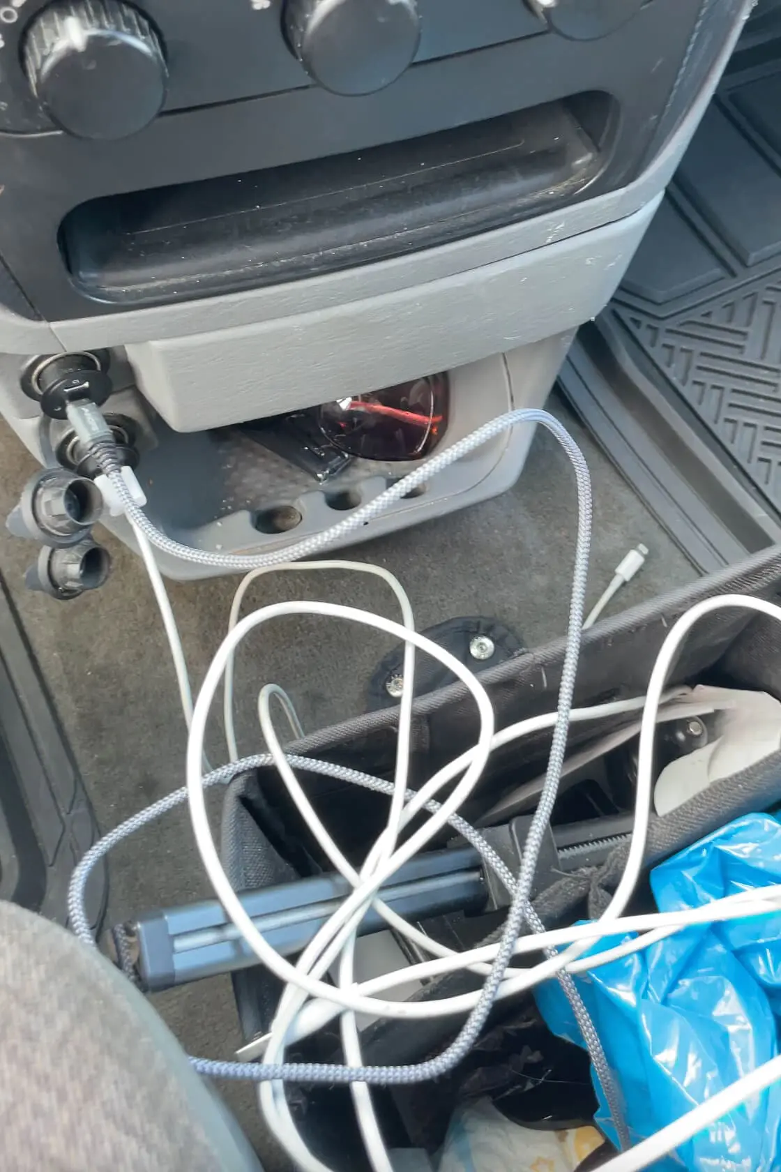 Tangle of phone cords and charging cables inside a car organizer on the floor near the center console, showing the reality of tech-packed road trips.