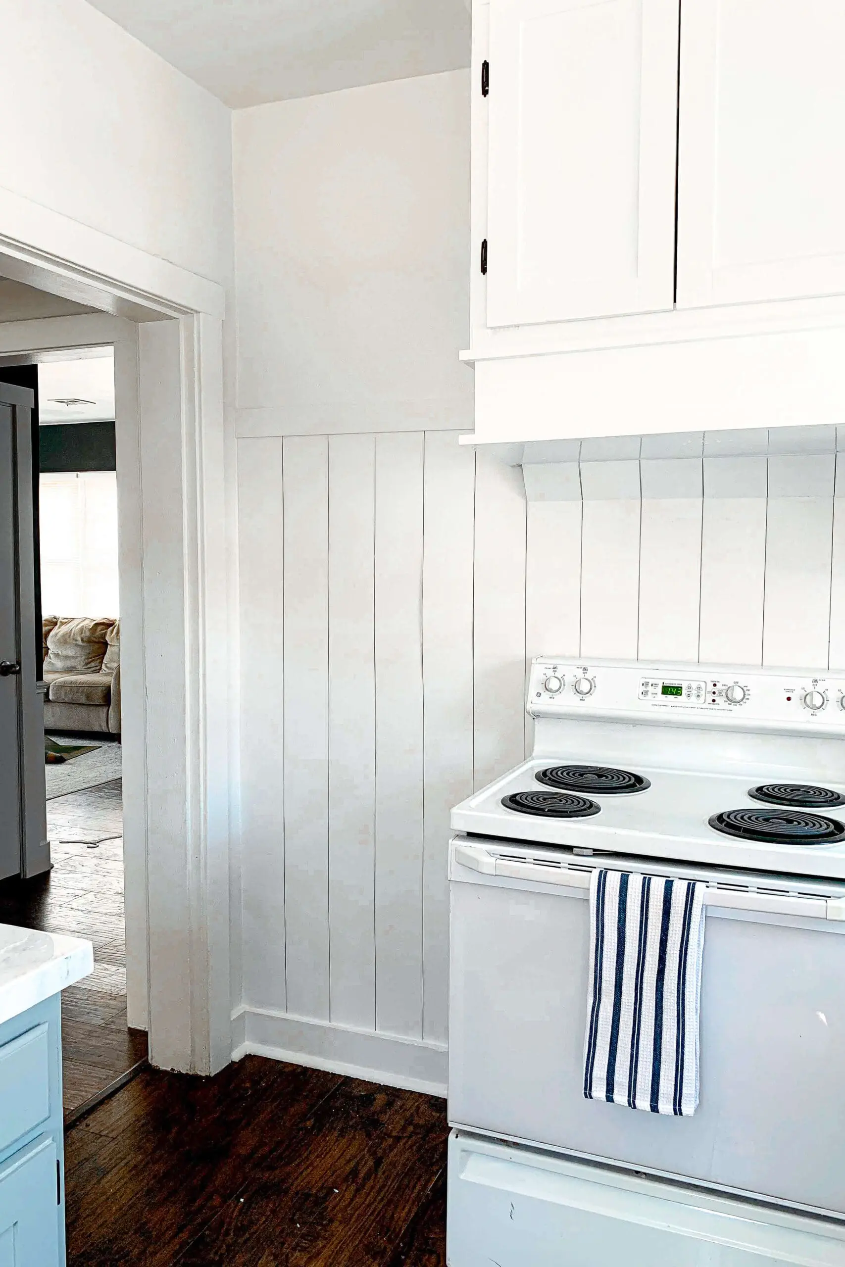 White shiplap accent wall in a bright kitchen corner with upper cabinets and a white stove, part of a budget-friendly DIY kitchen renovation project.