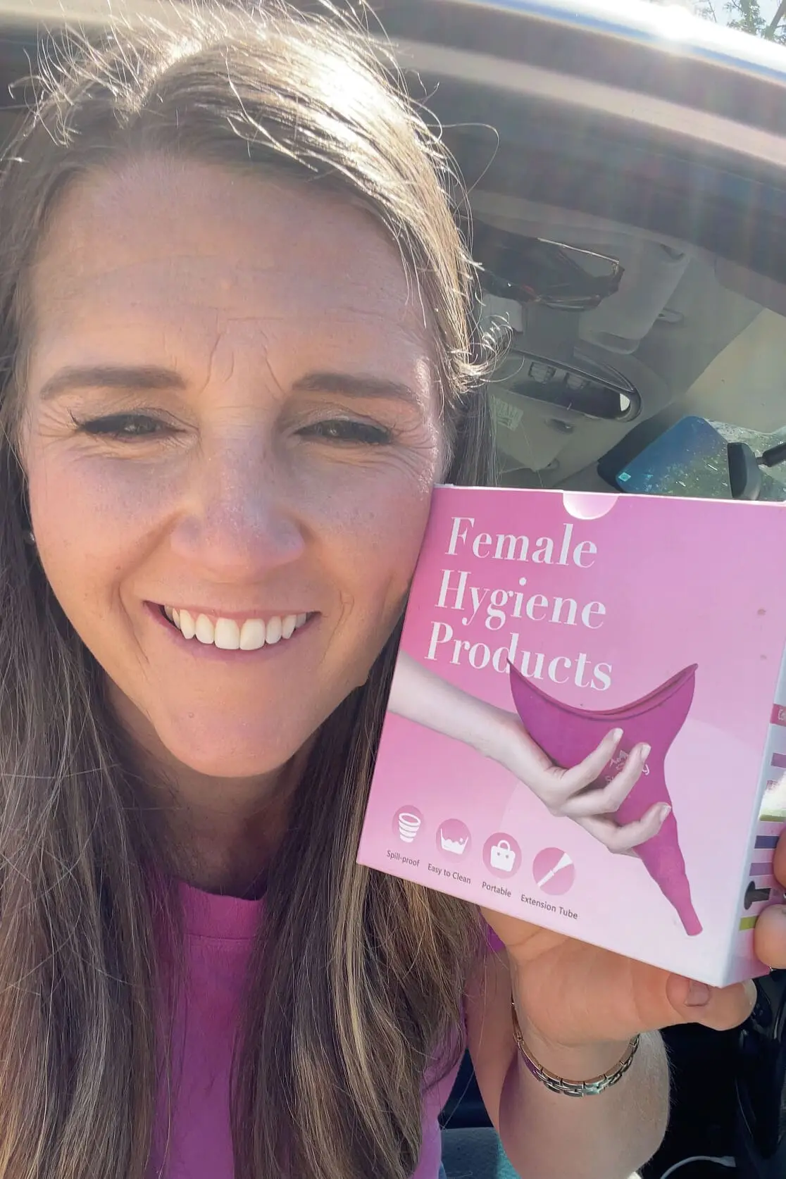 Woman smiling while holding a pink box labeled "Female Hygiene Products," sharing a helpful road trip essential for women.