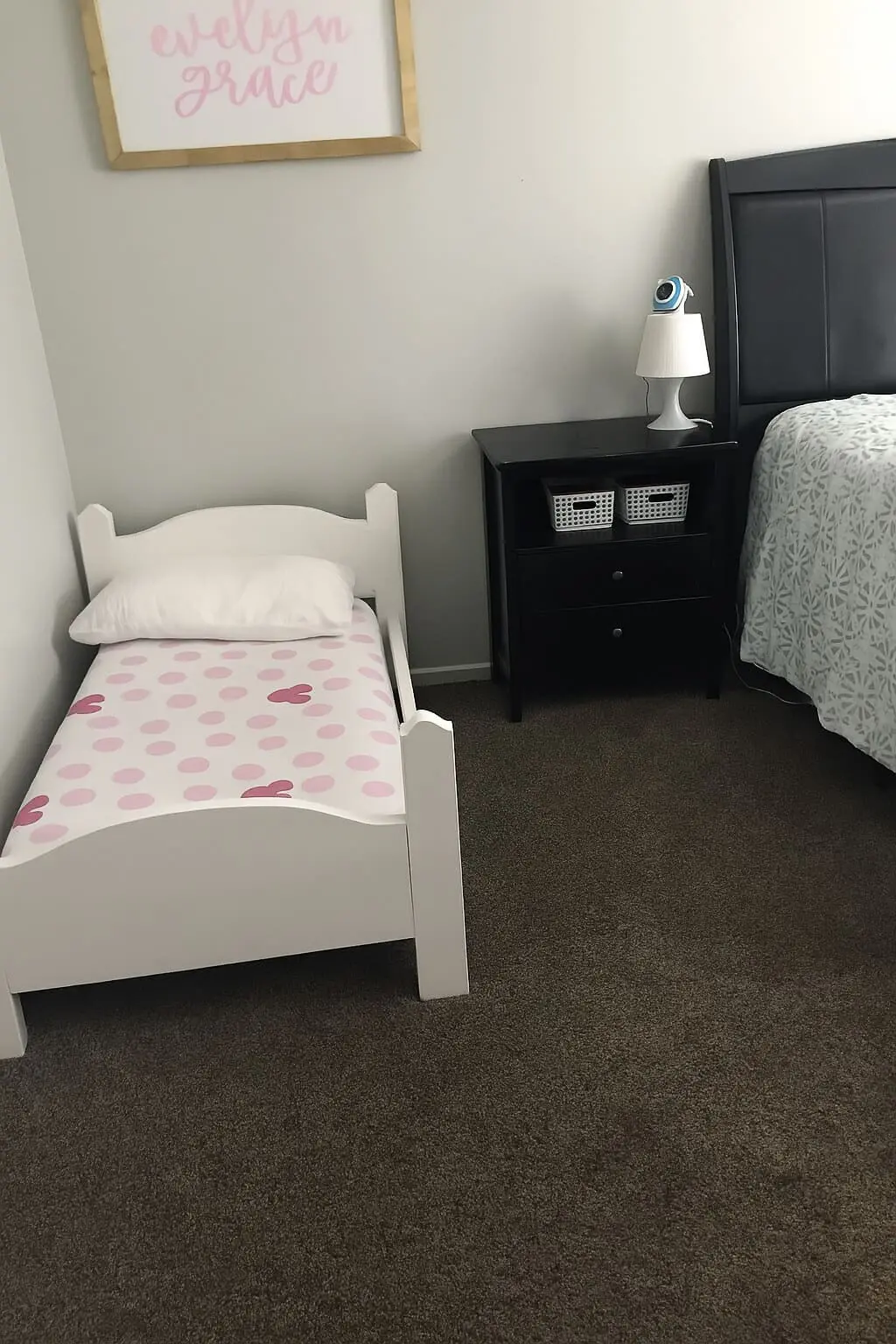 Finished DIY toddler bed painted white, styled in a shared bedroom setup with a nightstand and a larger bed nearby.