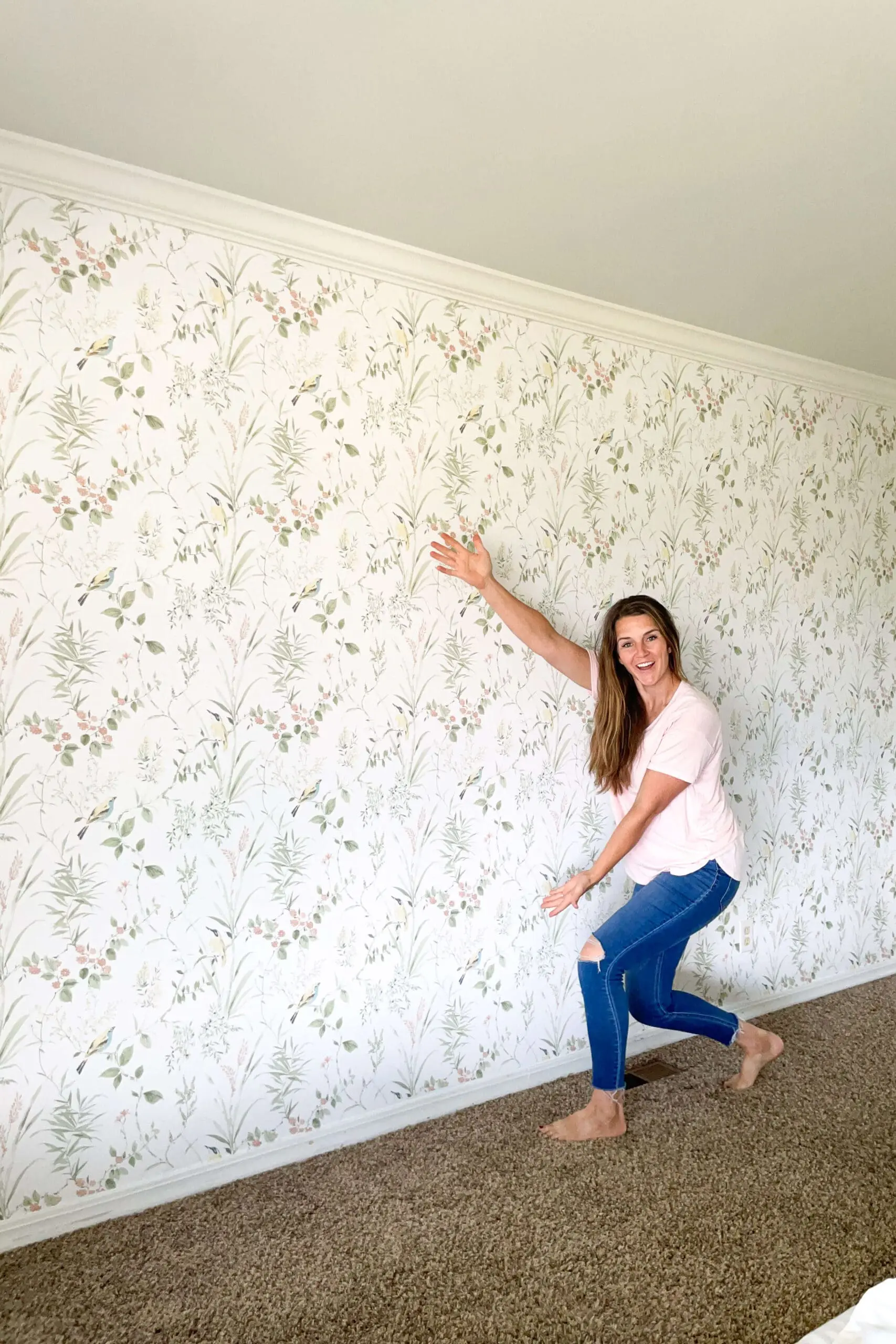 Smiling woman pointing to a freshly installed floral traditional wallpaper on a bedroom wall