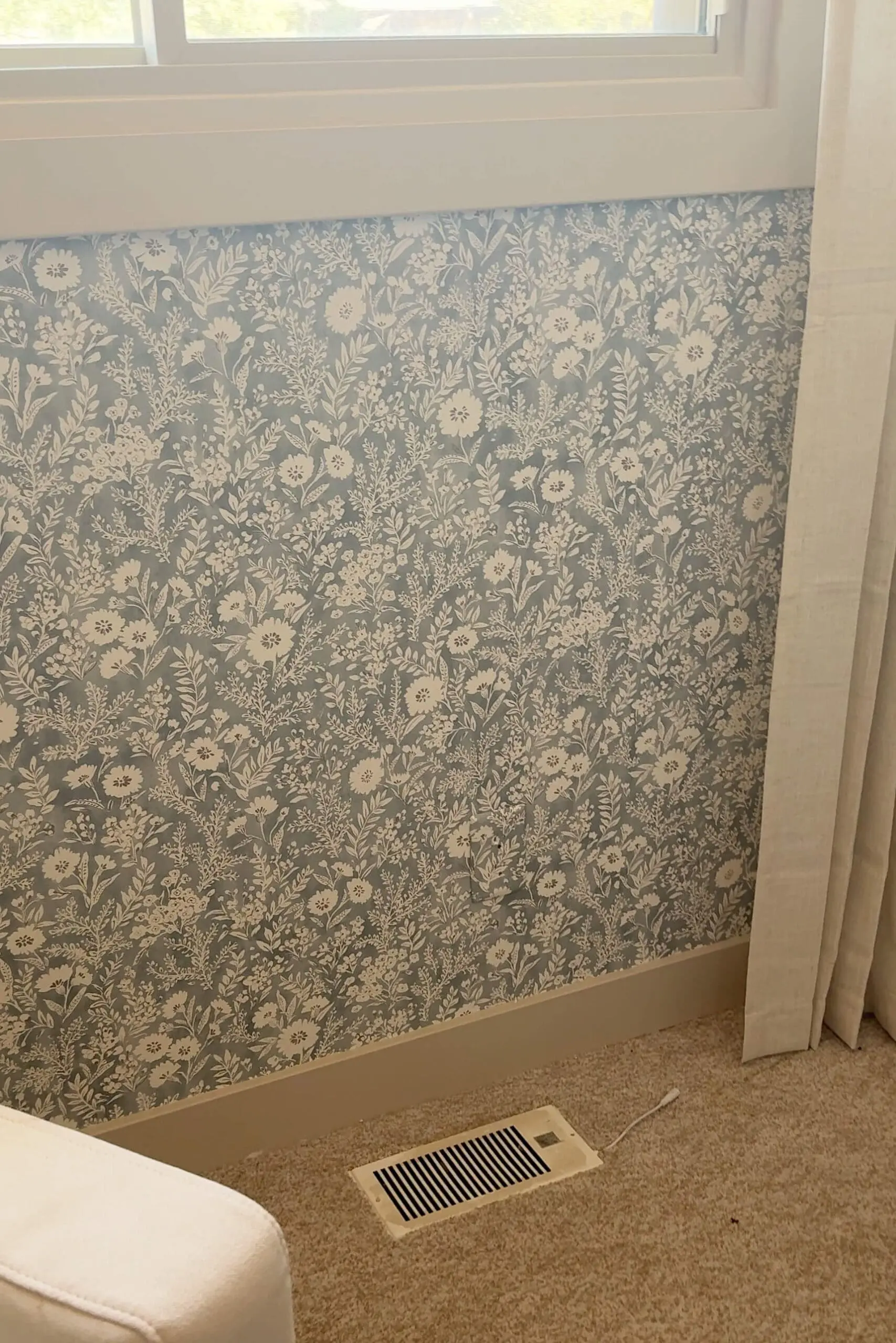 A full view of a wall covered in soft blue and white floral wallpaper with matching trim, showing how outlet covers disappear into the design.