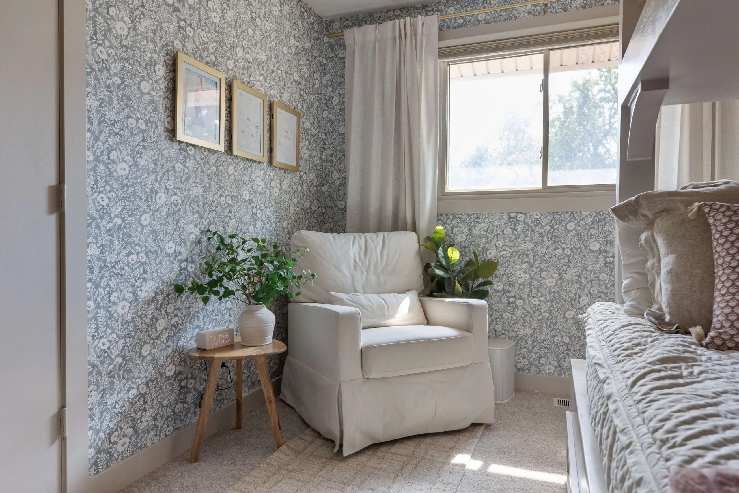 Light and airy bedroom corner with floral wallpaper, a cozy white armchair, layered textures, and neutral decor.