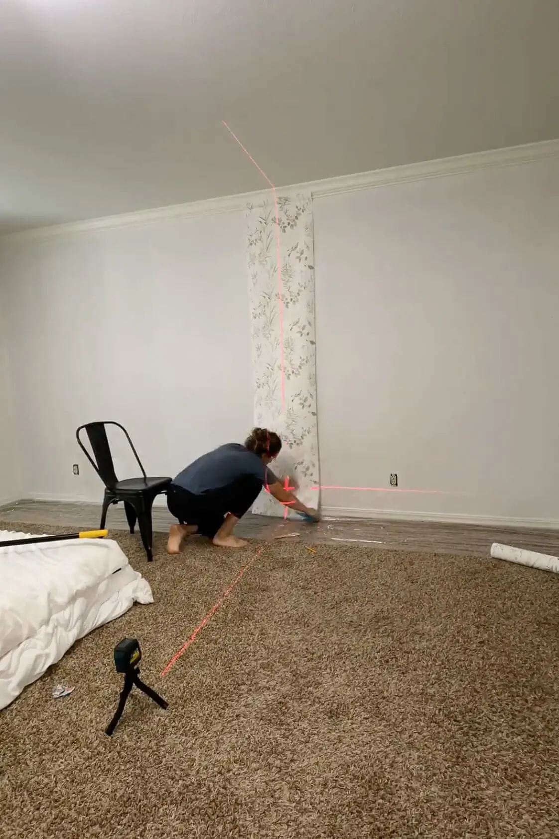 Applying the first panel of traditional wallpaper using a laser level for alignment