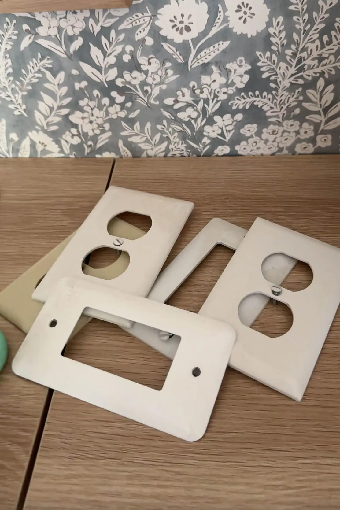 A pile of plain white and beige wall plates and switch plates laid out on a wood surface, ready for a DIY update.