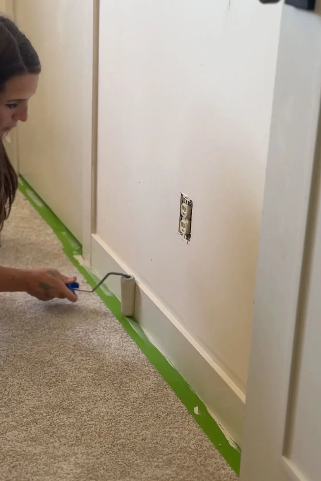 Painting the baseboards with a roller after laying painter’s tape to prep the room for the wall treatment installation.