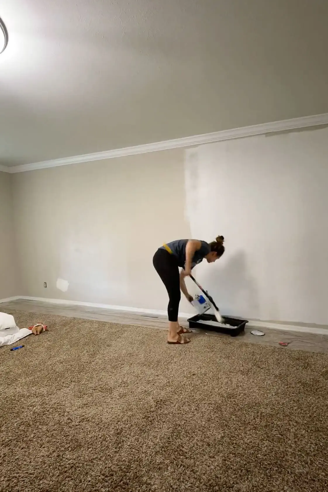 Woman loading a paint roller with white paint while prepping a bedroom wall