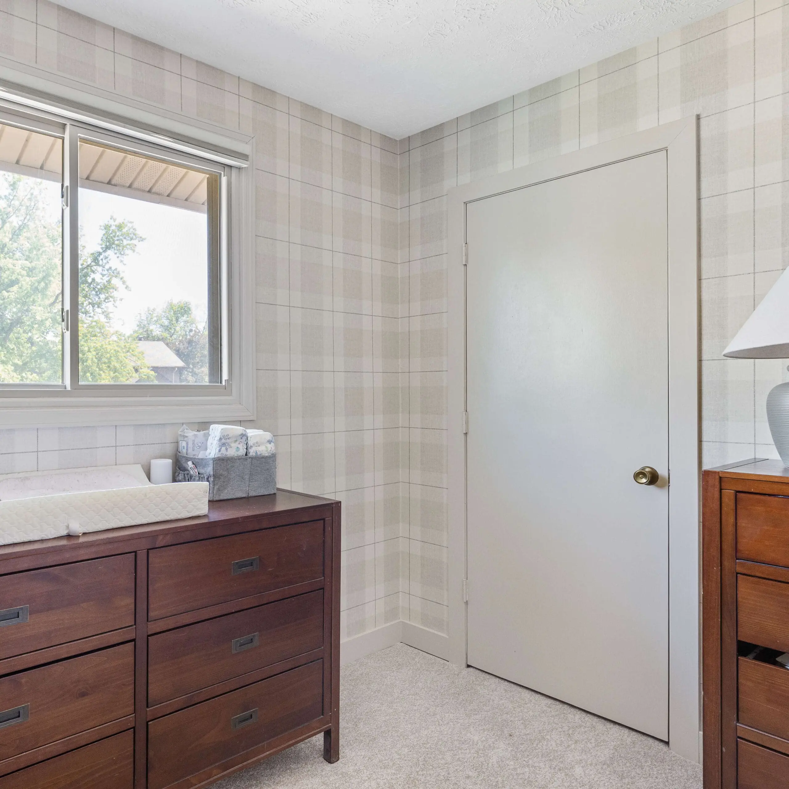 Neutral plaid peel and stick wallpaper installed in a nursery corner with wood furniture and soft beige trim.