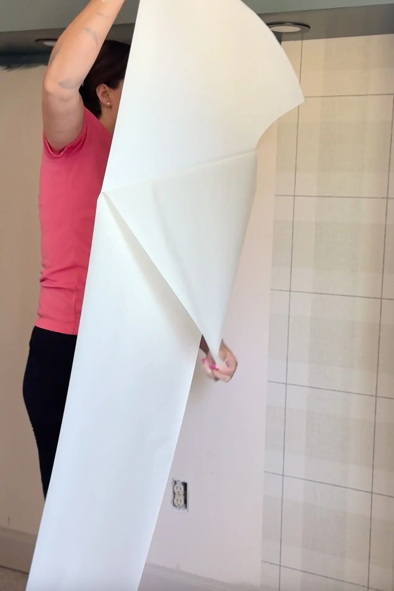Peeling the backing off a large sheet of wallpaper before aligning it on the wall during a plaid wallpaper install.