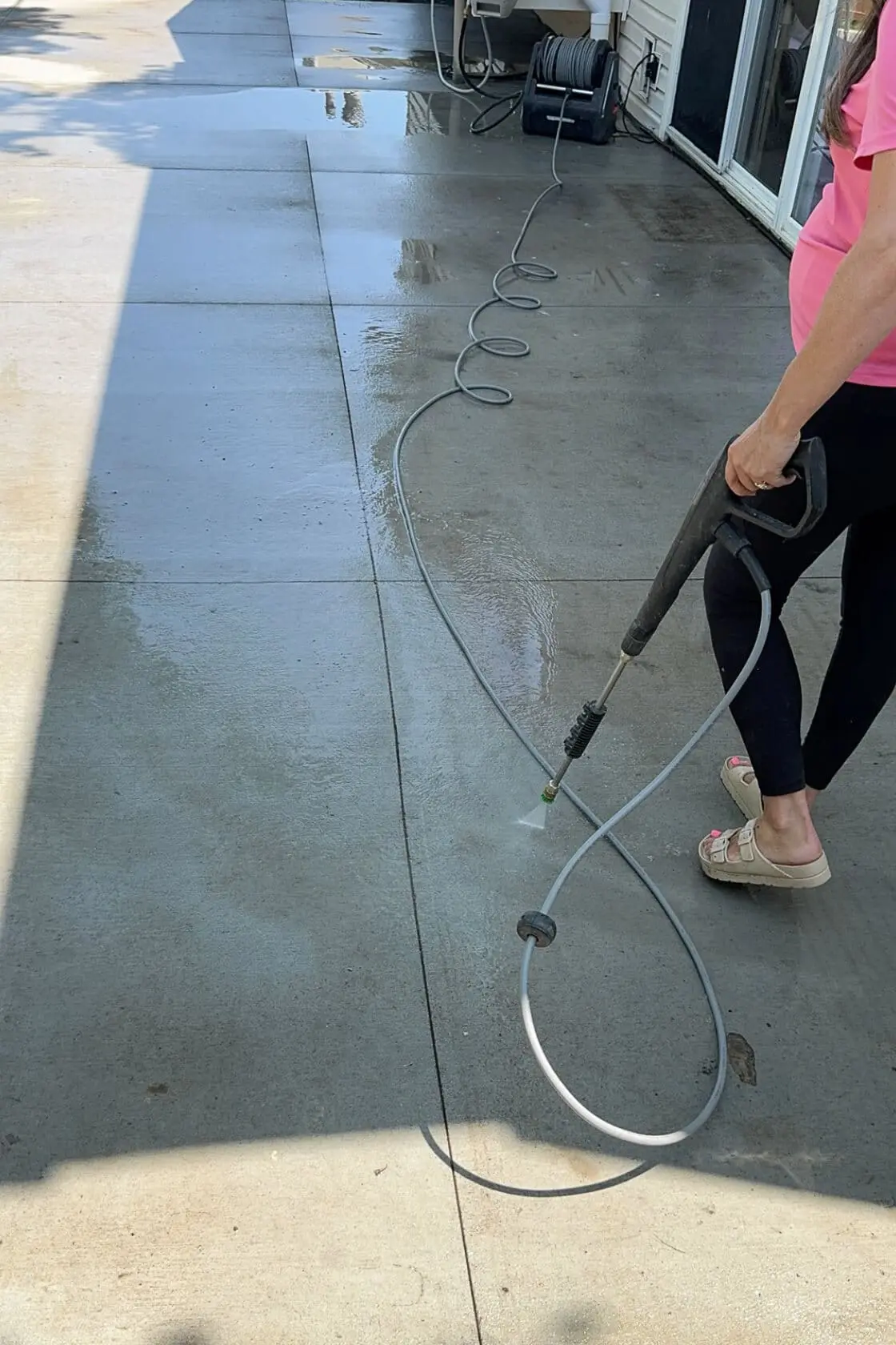 Woman pressure washing a backyard patio, cleaning dark buildup off the concrete surface