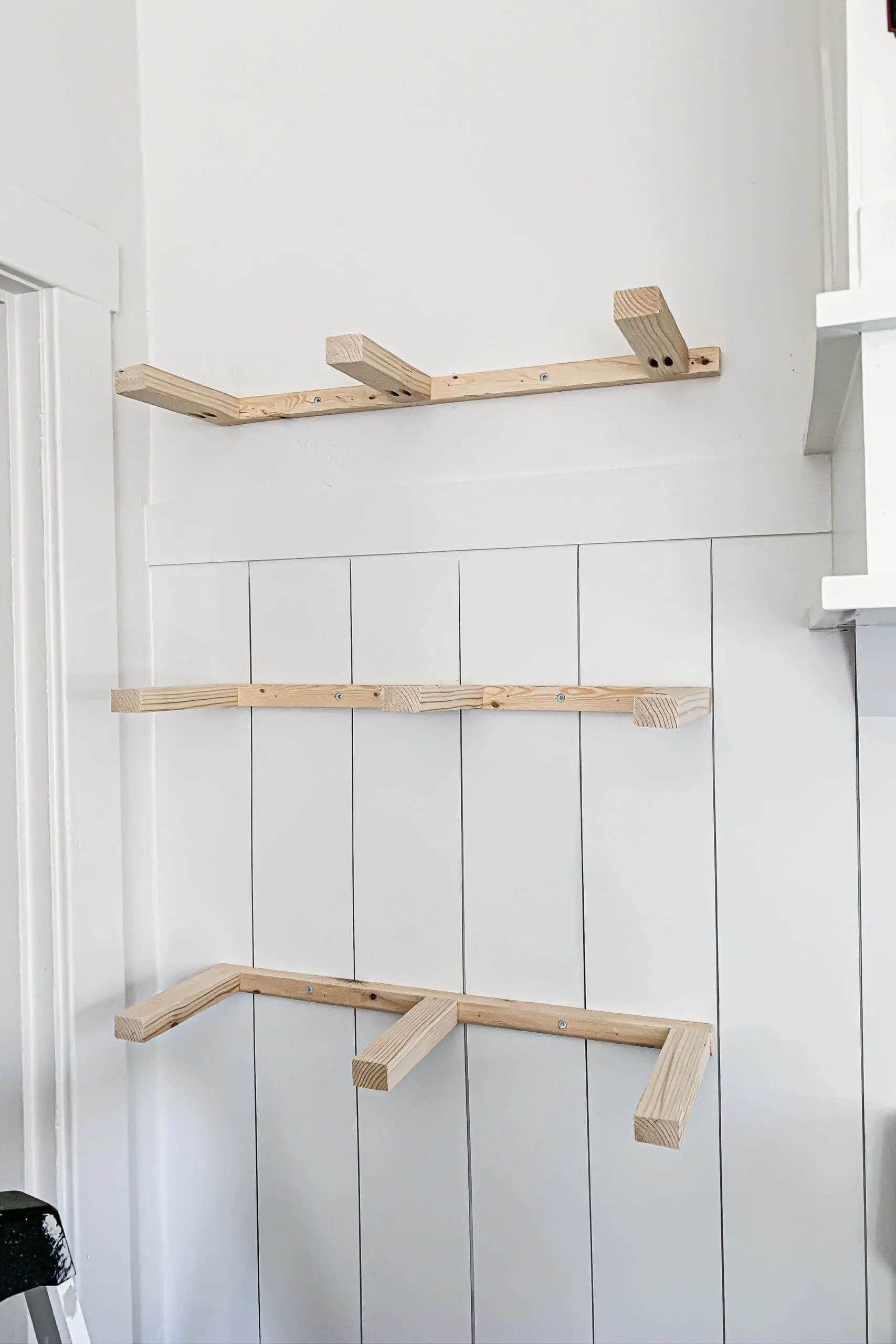 Three wooden shelf cleats installed on a white shiplap wall in a kitchen, showing the internal support structure for DIY floating shelves before the outer boards are added.