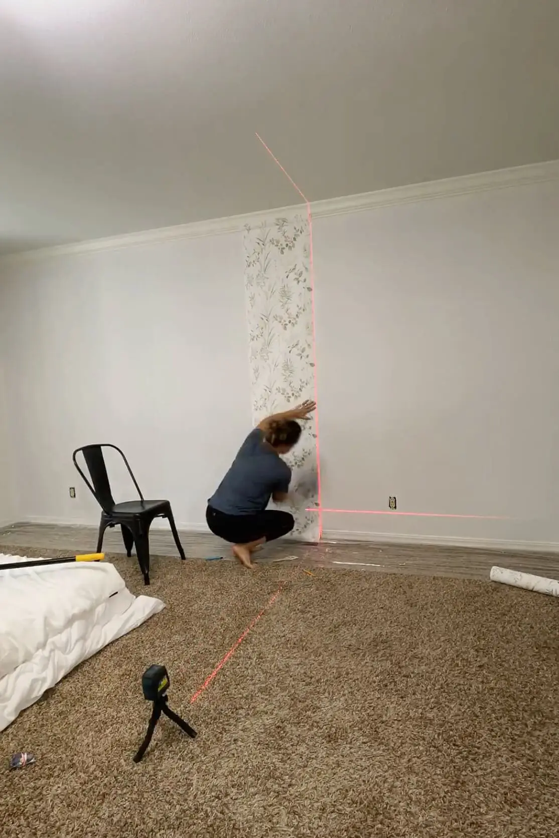 Smoothing a panel of traditional wallpaper onto the wall while using a laser level for precision