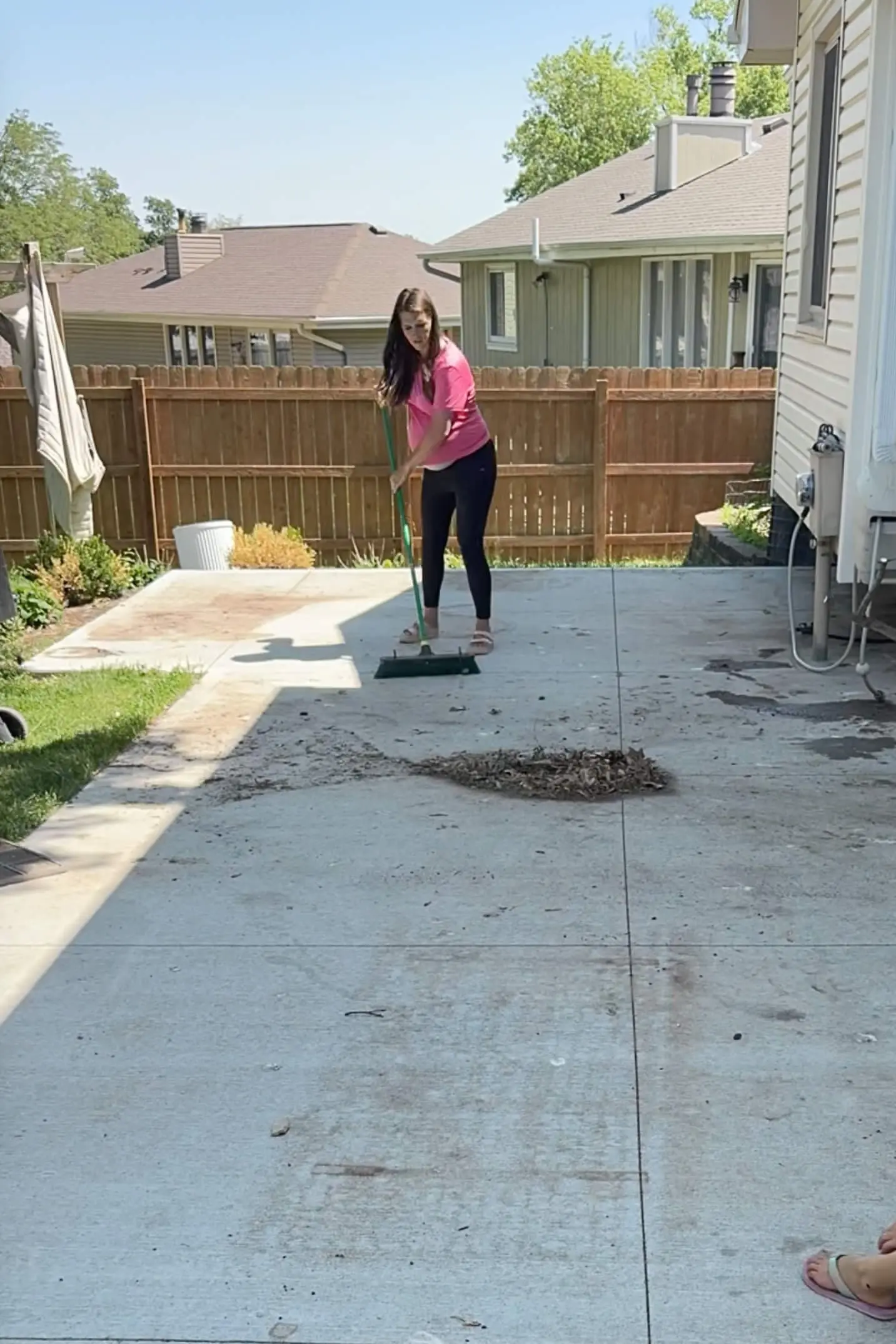 Woman sweeping leaves and debris off a backyard patio during outdoor summer prep.