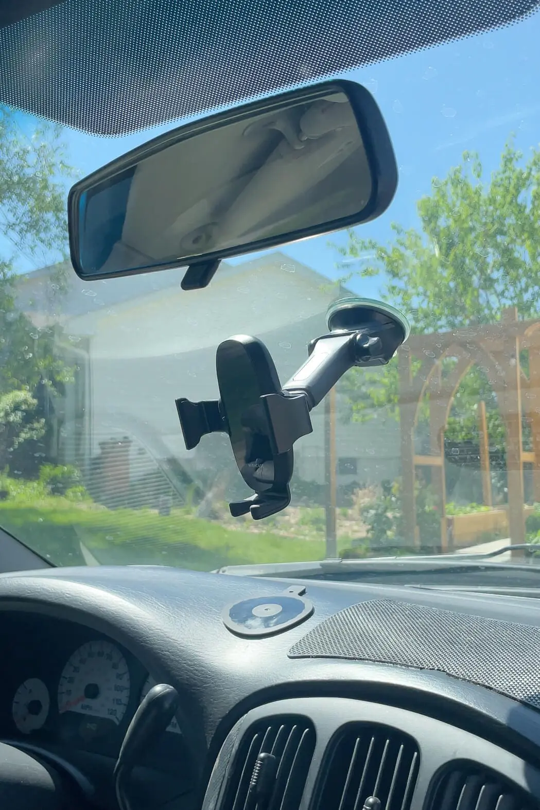 Suction-cup style phone holder attached to the car windshield next to the rearview mirror, ideal for hands-free navigation.