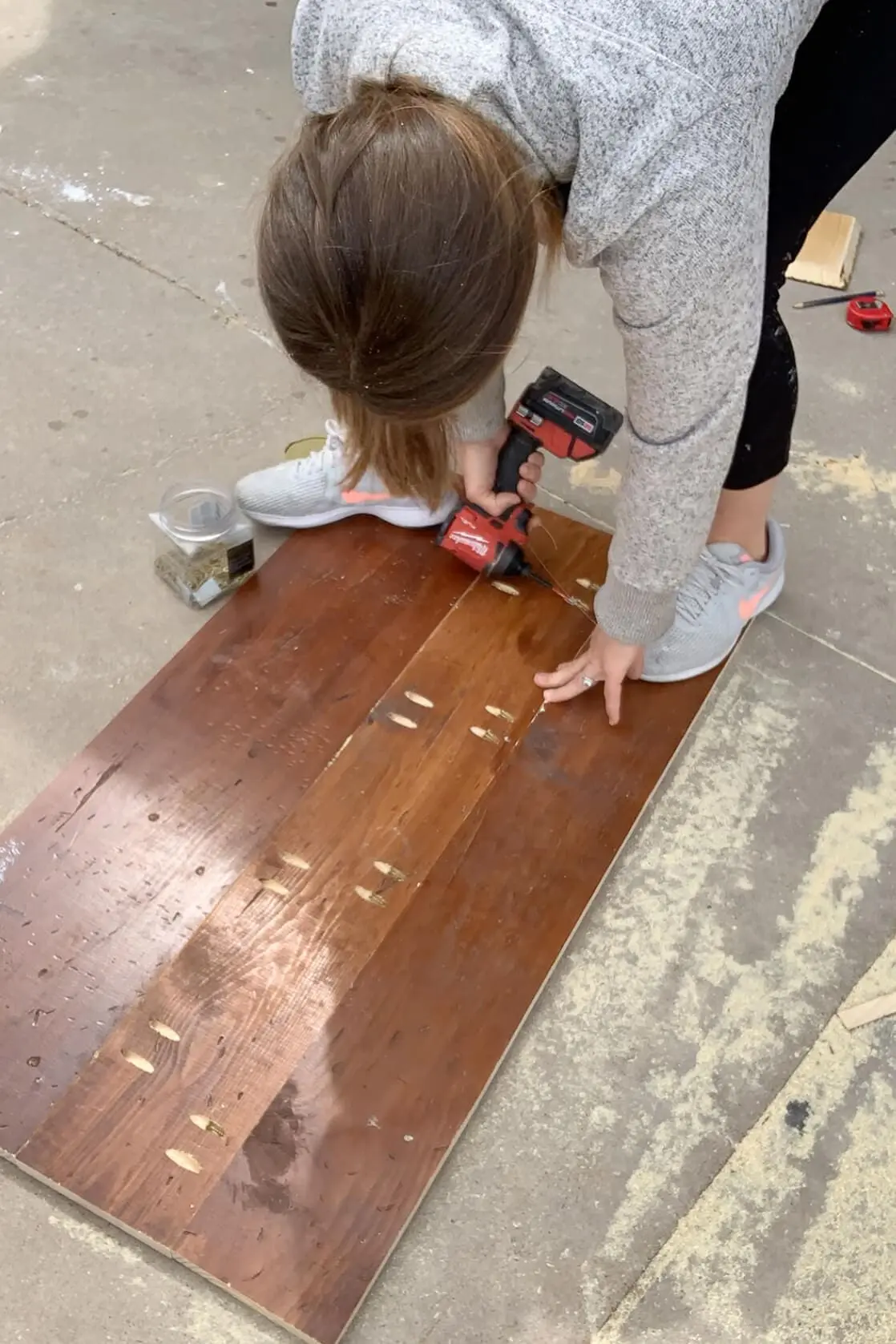 Using a drill to assemble pocket hole joinery in repurposed wood boards during tabletop construction.